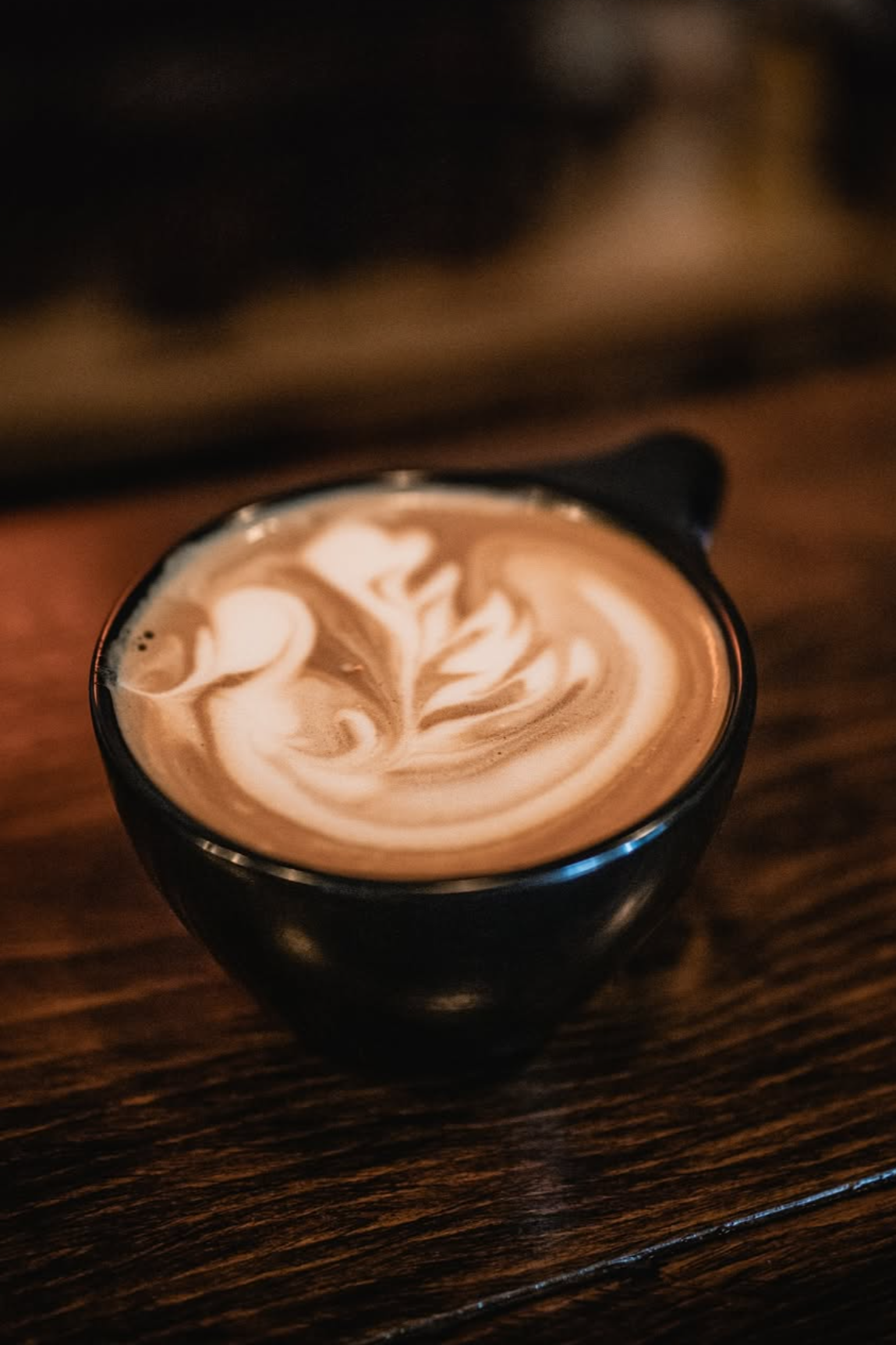 A close-up photo of a black coffee cup filled with latte art on a wooden table.