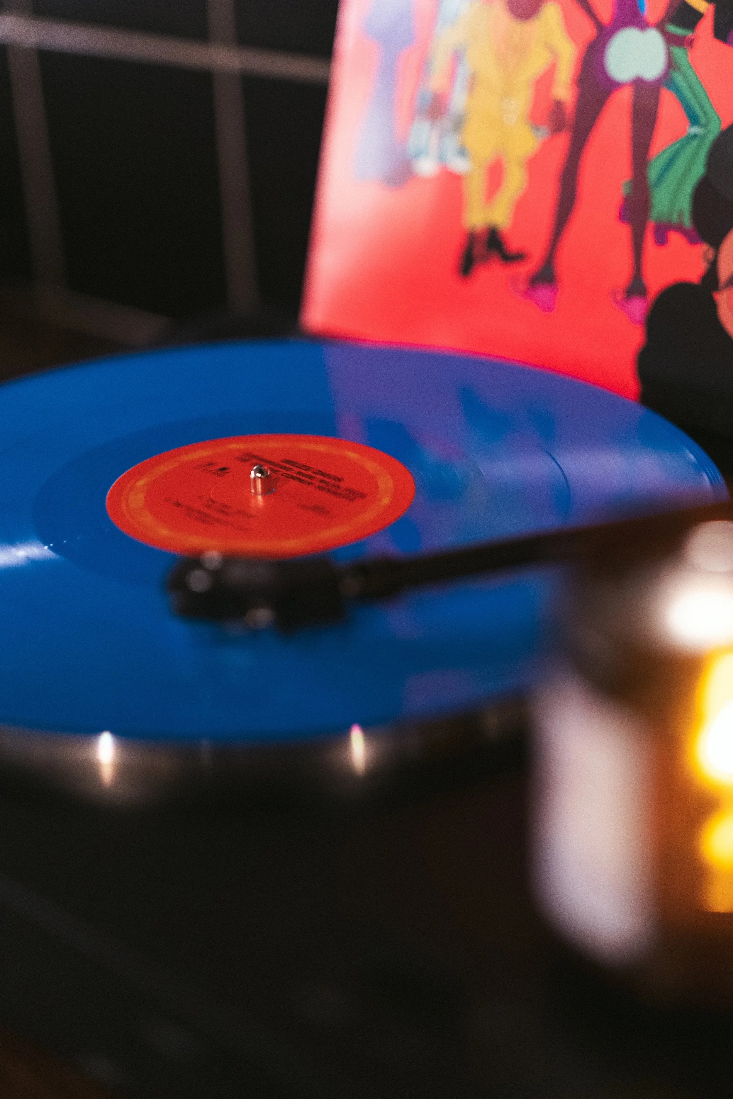 Blue vinyl record spinning on a turntable with a red label at the center, in front of a colorful album cover with cartoon characters.
