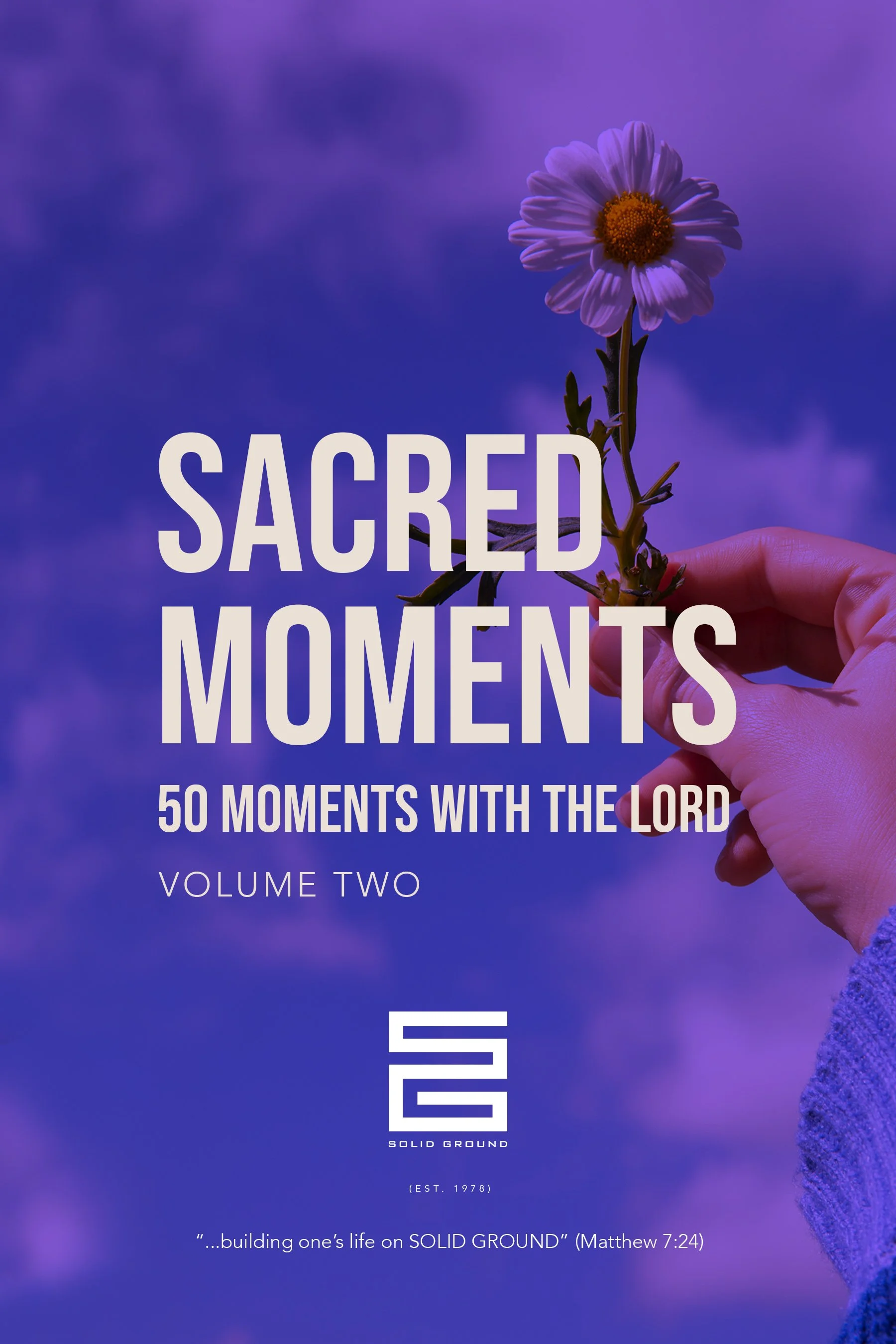 Close-up of a hand holding a daisy flower against a purple sky background with the title 'Sacred Moments' and the subtitle '50 Moments with the Lord, Volume Two' overlaid on the image.