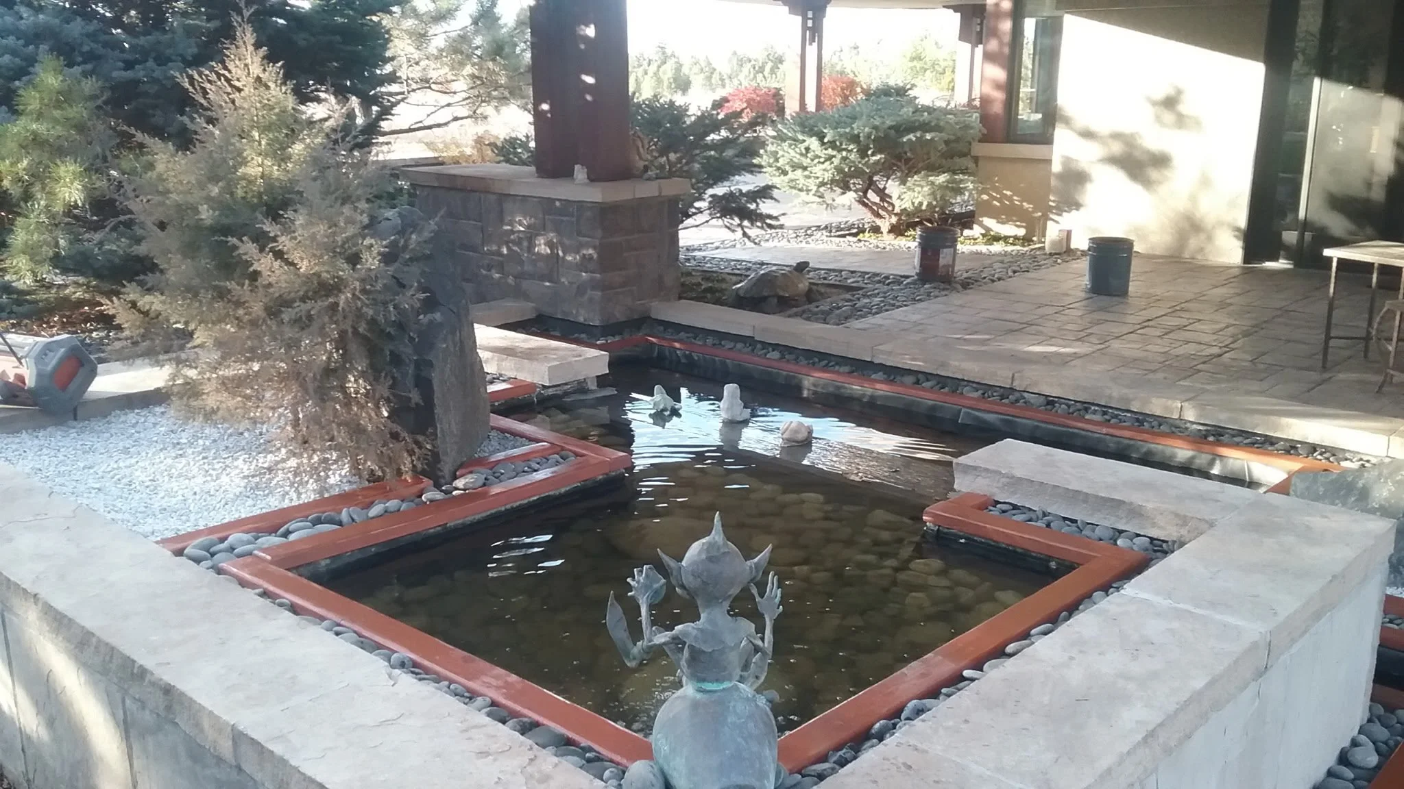 Decorative outdoor fountain with sculptures of a frog and ducks, surrounded by rocks, plants, and a patio area.