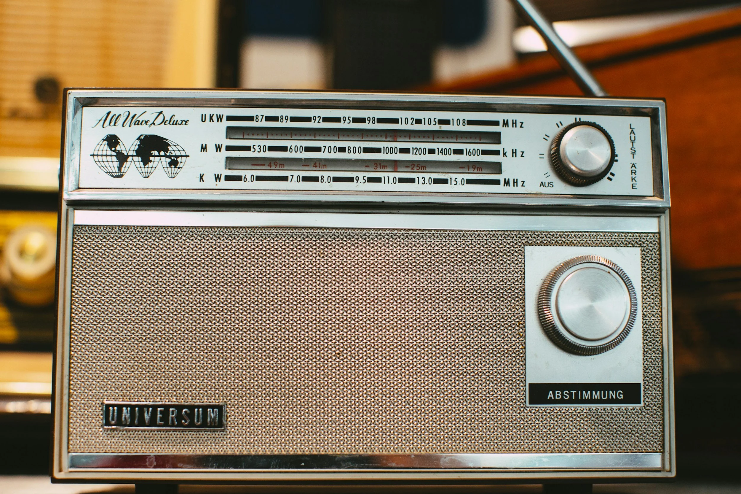 Vintage radio with a silver metallic finish, featuring tuning dial, volume knob, and a frequency display with world map illustrations.