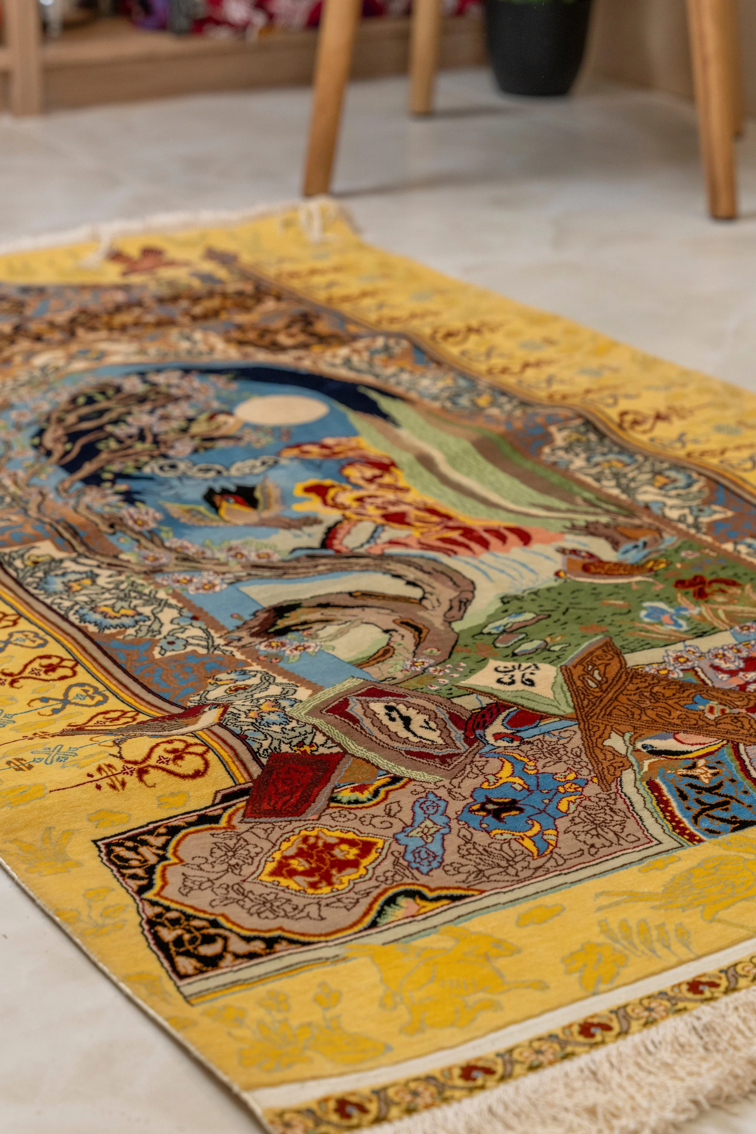 Close-up view of a colorful, intricate rug laid out on a floor with part of a wooden chair and a black pot in the background.