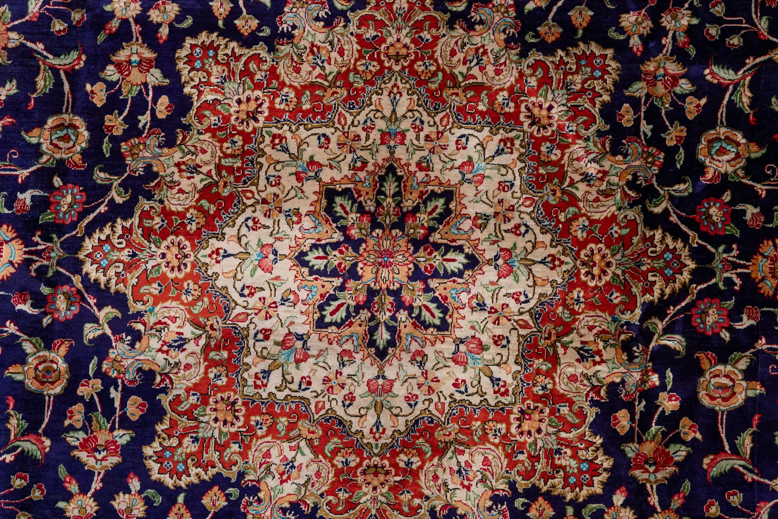 A traditional Persian-style rug with an intricate floral design in shades of red, cream, navy blue, and green.