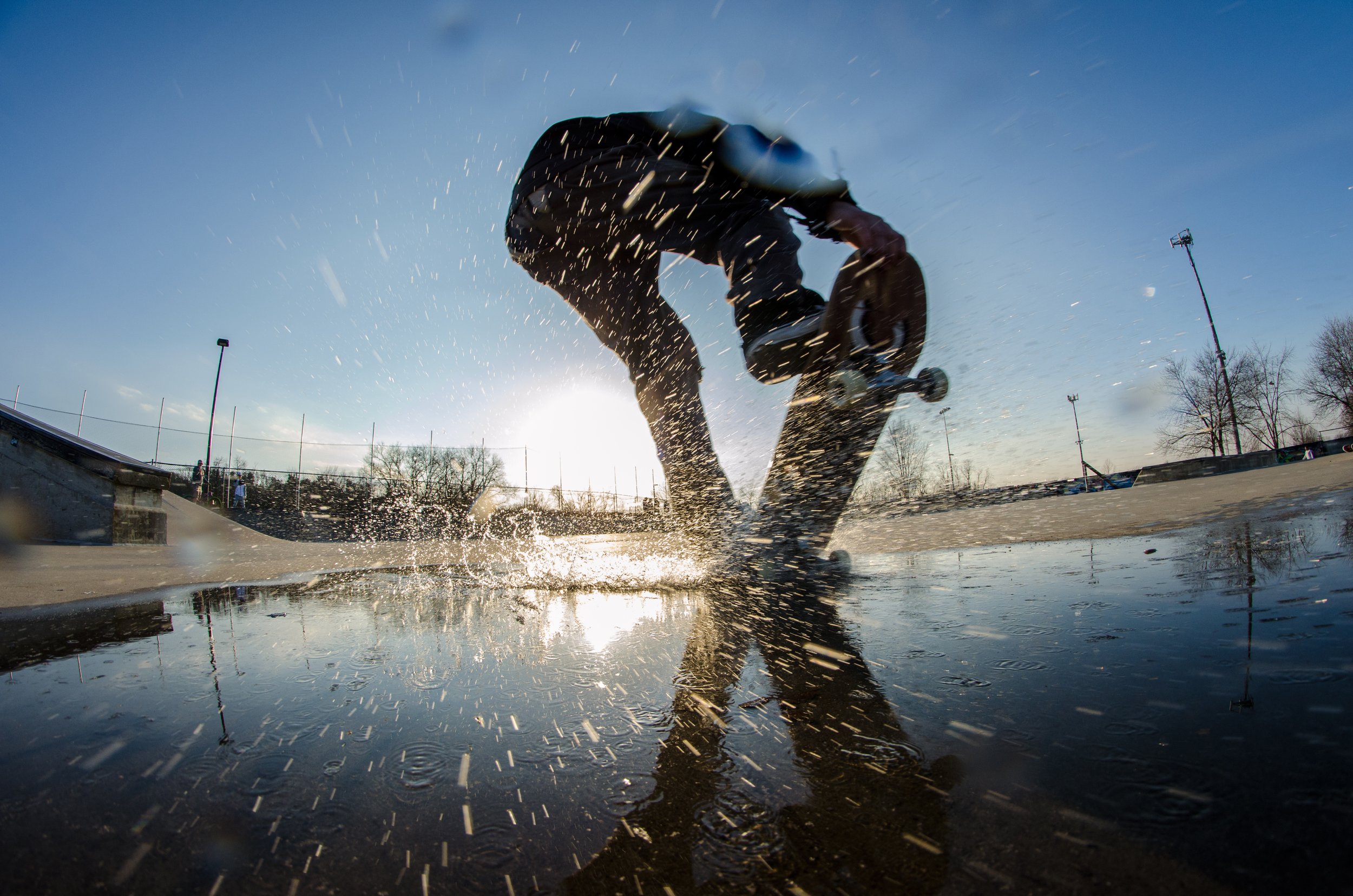 Skateboarder performing an ollie at a skatepark during sunset, with water on the ground splashing around