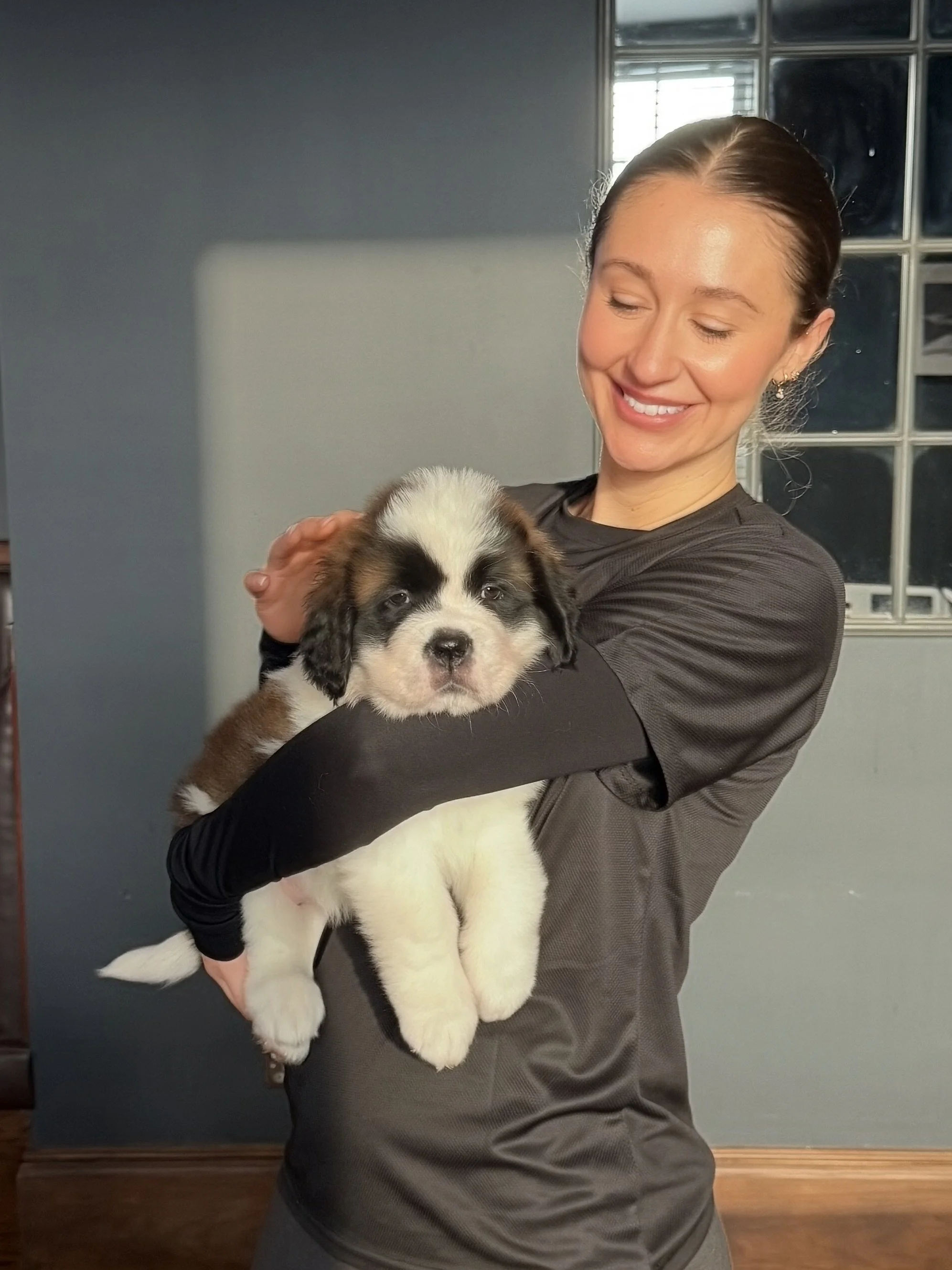 A woman smiling and holding a cute, fluffy puppy.