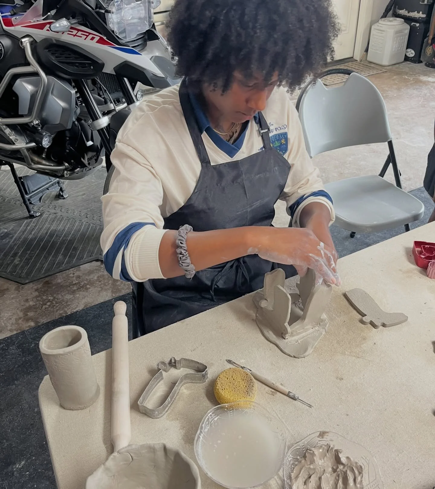 A woman working on a pottery sculpture at a table covered in clay and pottery tools.