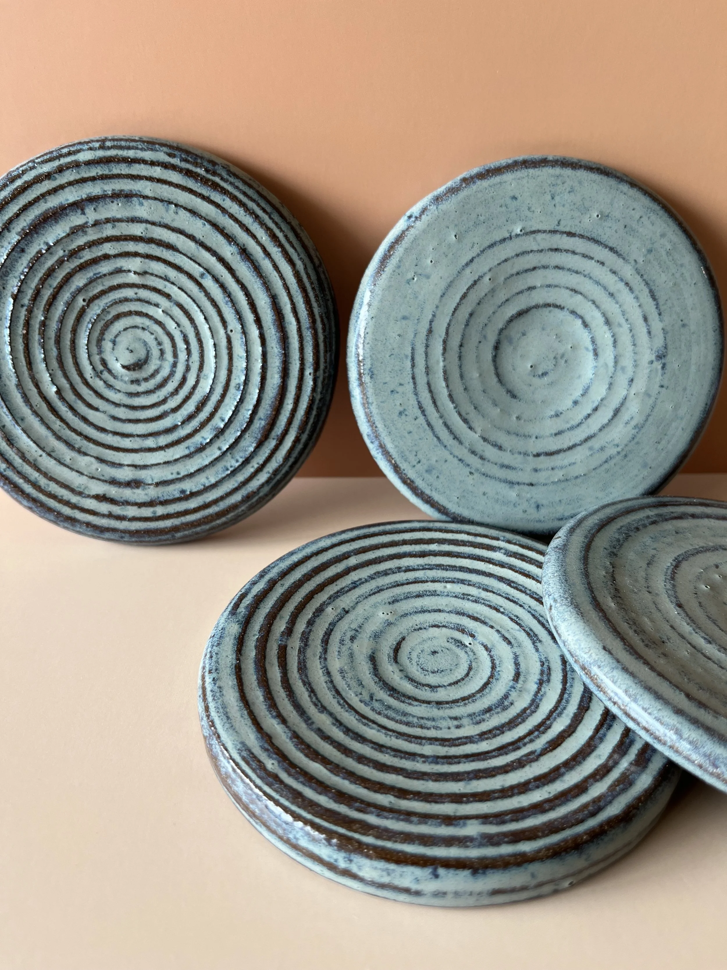 Close-up view of four ceramic bowls with blue and brown spiral patterns on a peach-colored and beige background.