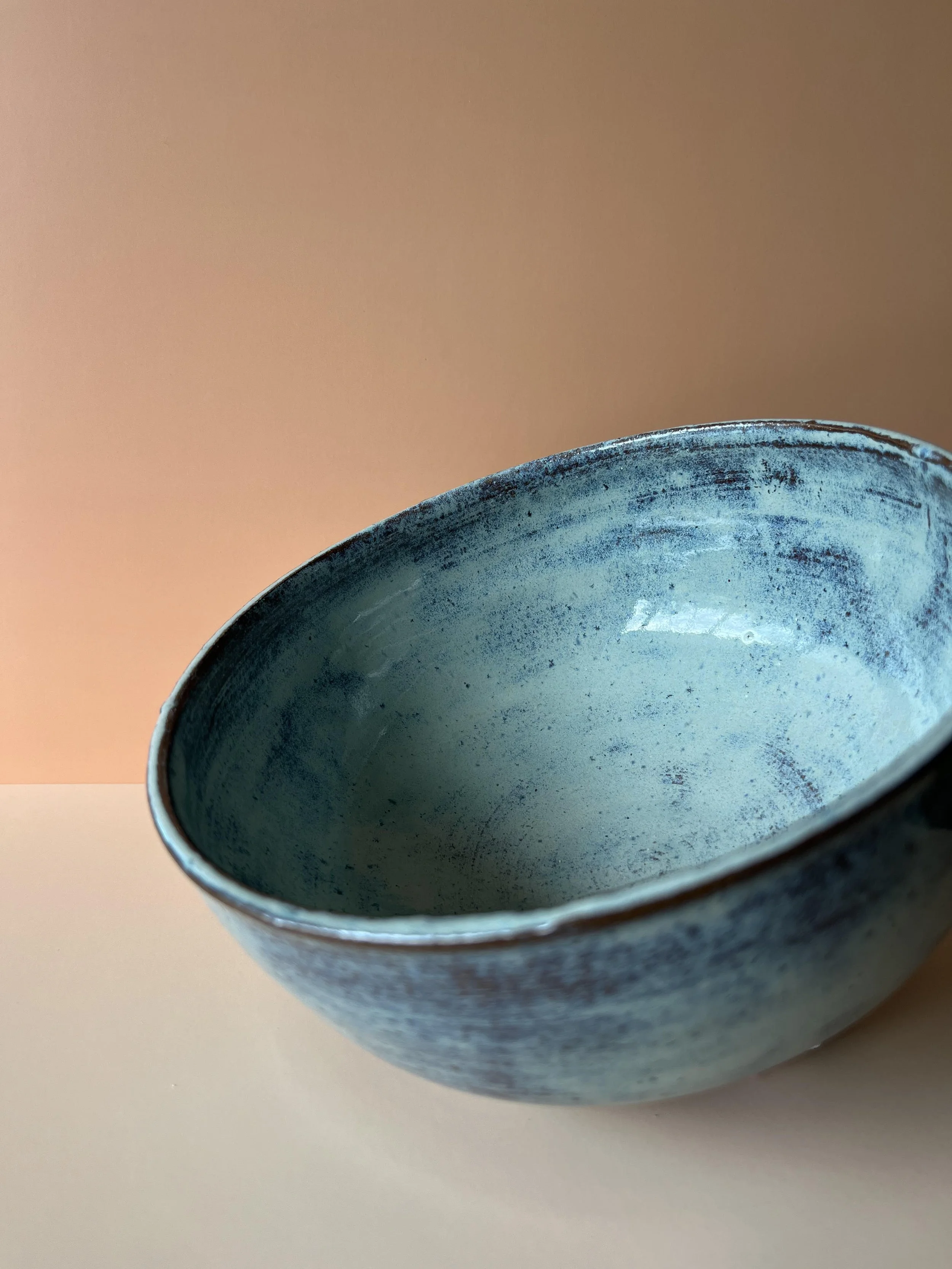 Close-up of a blue ceramic bowl with a textured glaze, placed on a white surface against a gradient background transitioning from peach to beige.