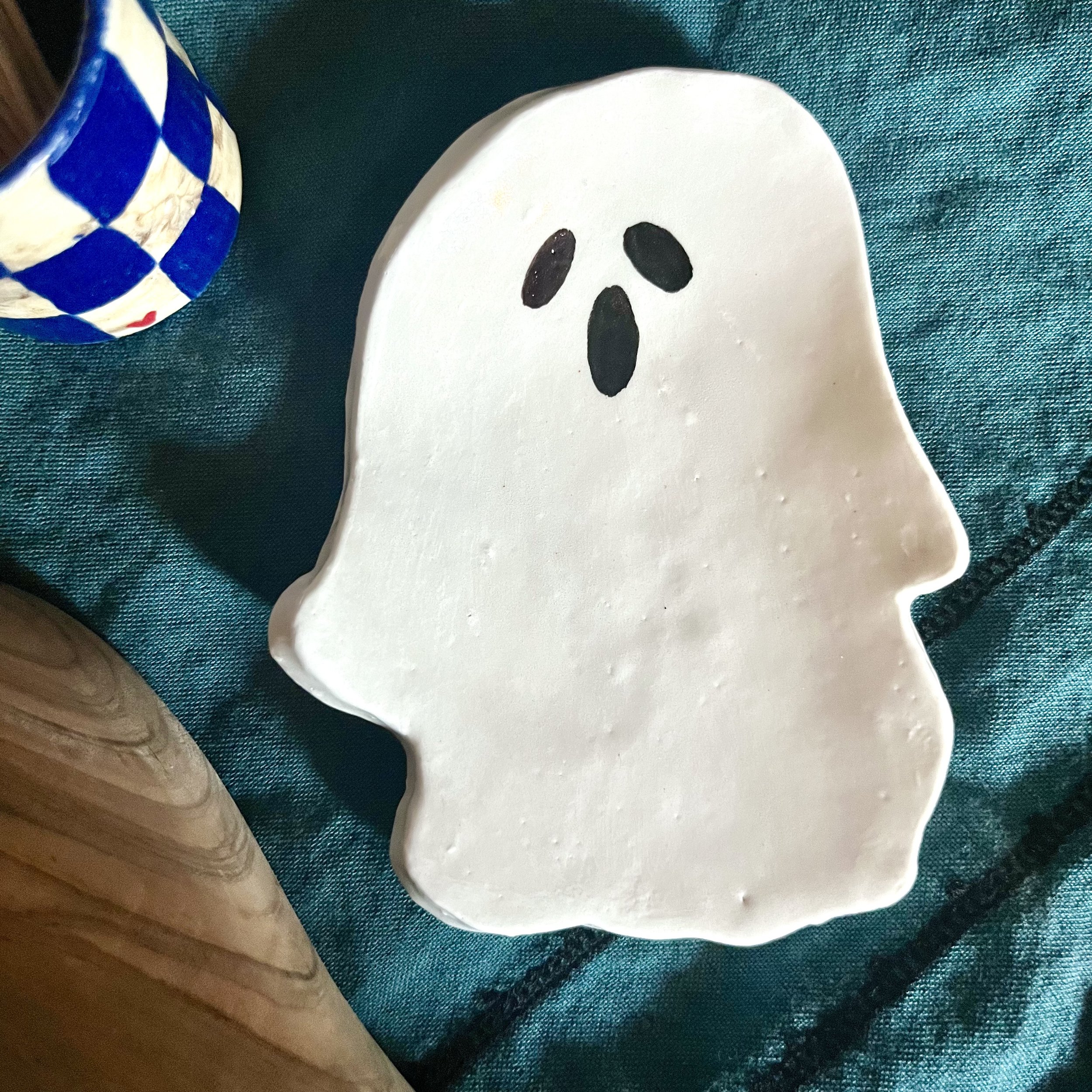 A white ceramic plate with a ghost face made of black paint, placed on a teal fabric surface.