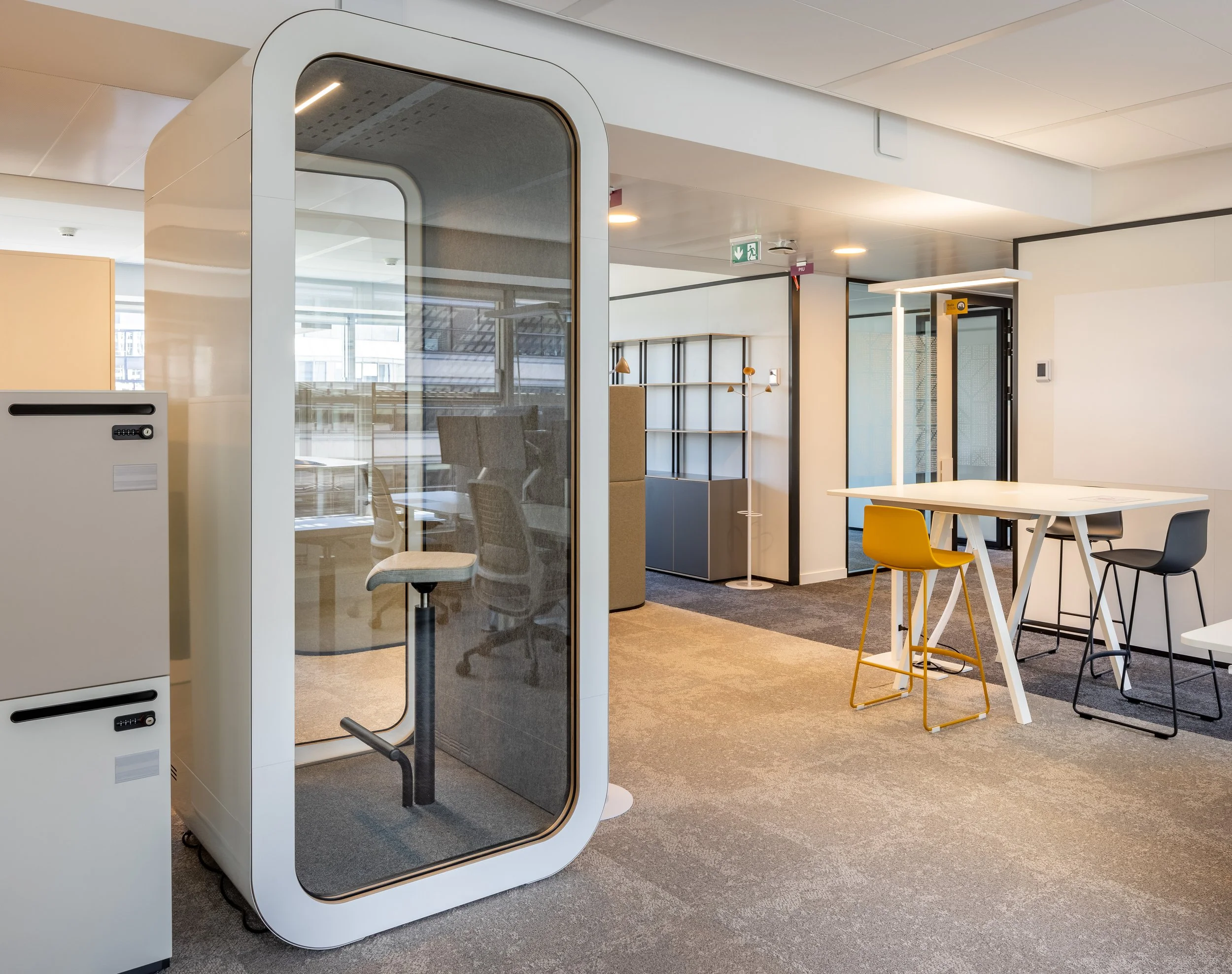 Espace de bureau moderne avec cabines de réunion individuelles, tables, chaises colorées, étagères et éclairage naturel