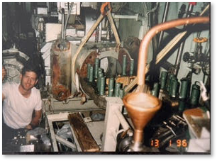 A man working with industrial machinery, surrounded by pipes and equipment in an industrial setting.