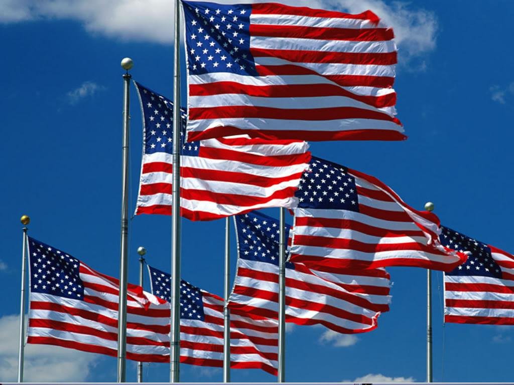 Multiple American flags waving in the wind against a partly cloudy sky.