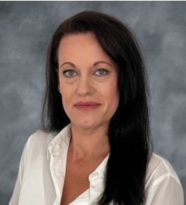 Portrait of a woman with long dark hair wearing a white blouse against a gray background.