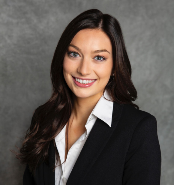 Professional woman with long dark hair, blue eyes, wearing a black blazer and white shirt, smiling against a gray background.