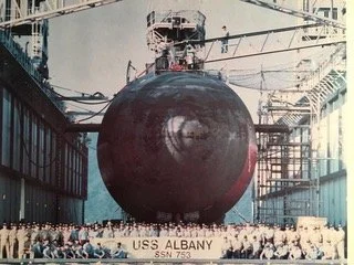 The USS Albany submarine in a dry dock with workers and scaffolding around it.
