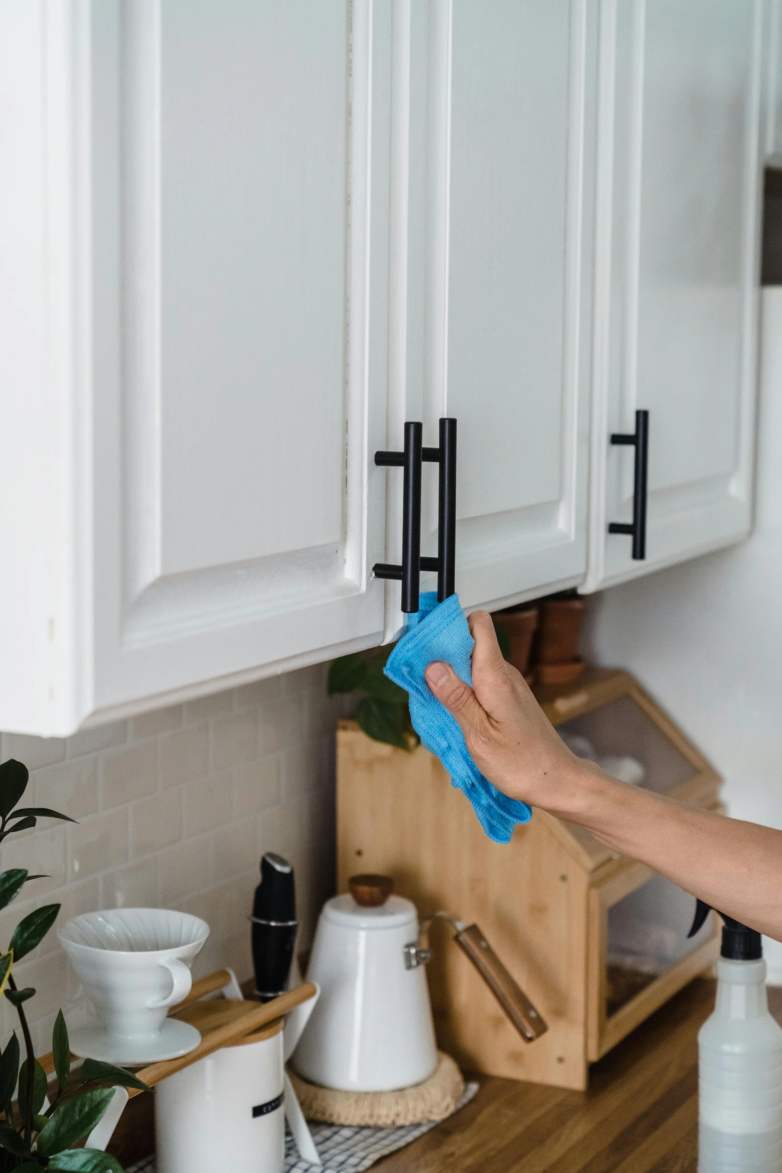 Hand wiping black cabinet handles with a blue cleaning cloth in a kitchen.