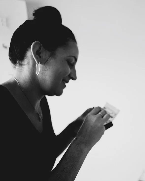 A woman with dark hair tied in a bun, wearing earrings, looking at her smartphone and smiling.
