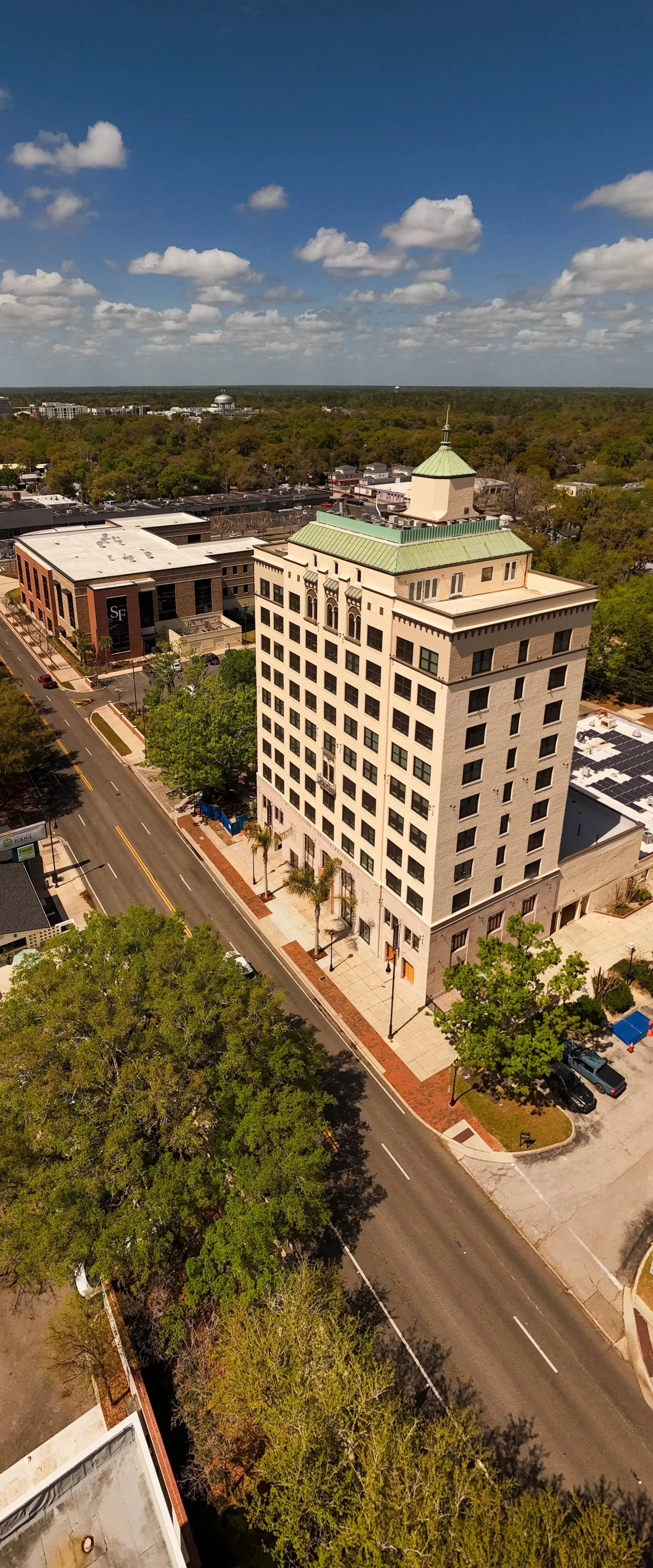 A vertical panoramic of the Seagle Building, a historic white building with a green roof and a small tower on top, surrounded by trees and a city street.