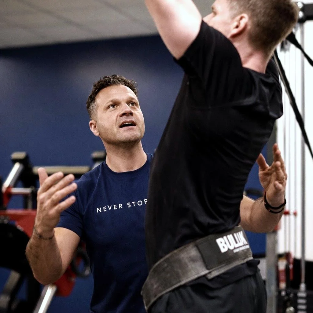 A personal trainer instructs a man during a workout at a gym.