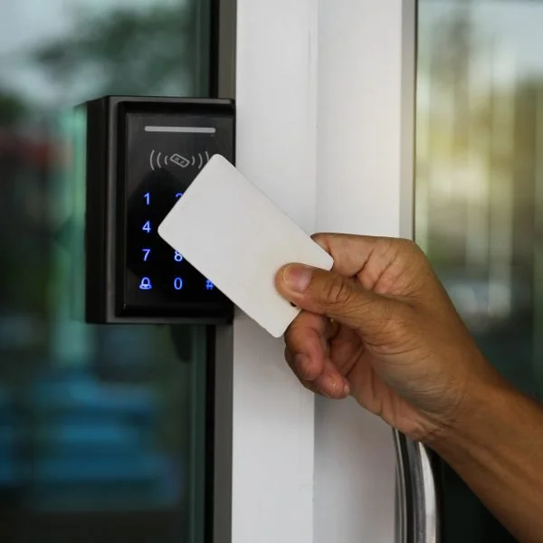A person holding a white card near an electronic access control keypad to unlock a door.