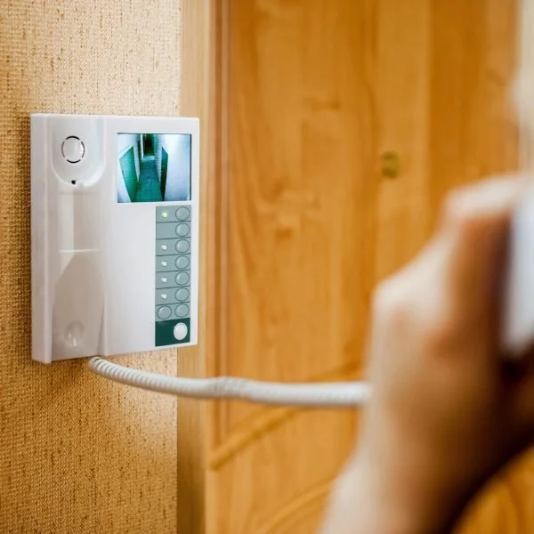 Person holding a phone to an intercom device with a small screen showing an outdoor corridor.