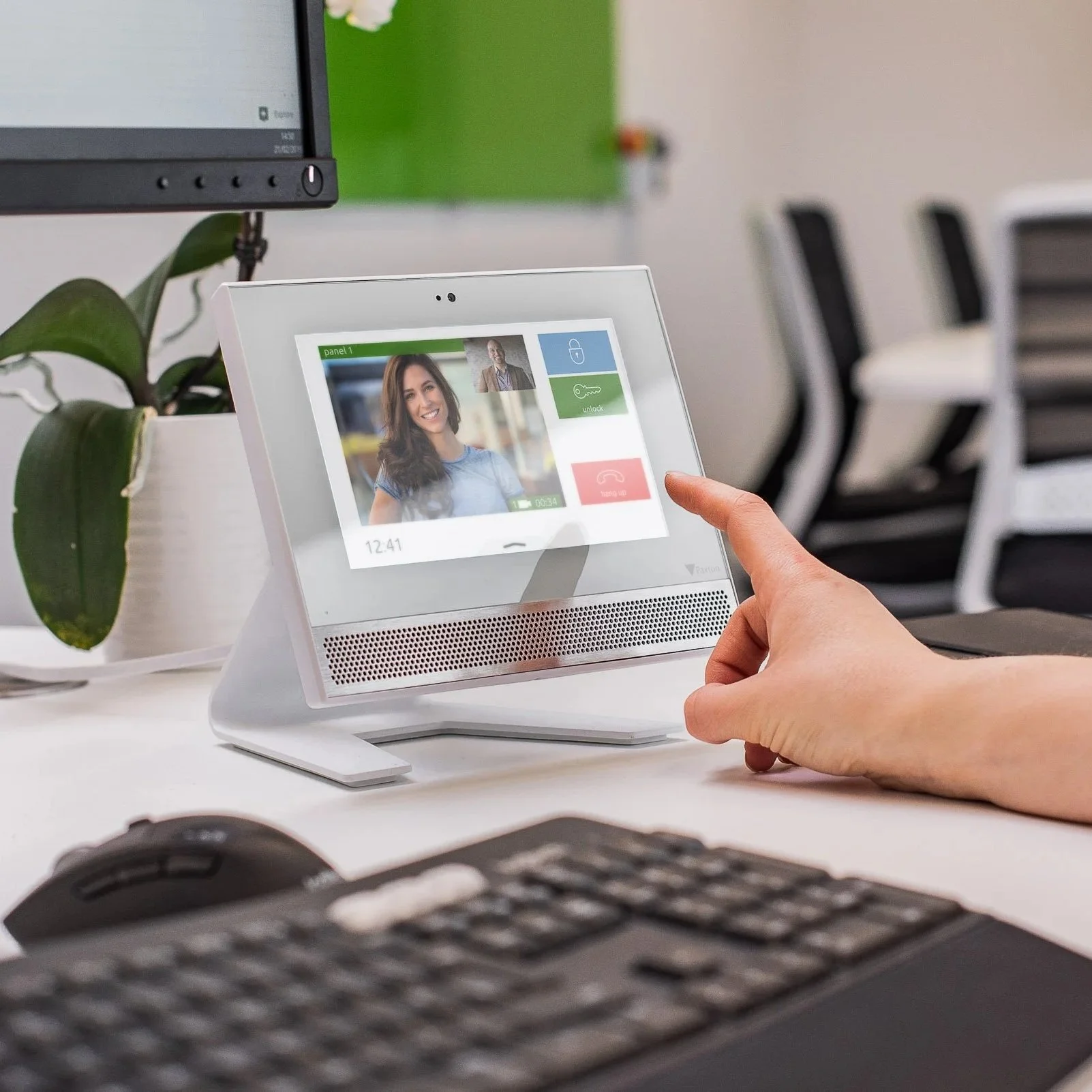 A person using a video intercom device in an office setting. The screen shows a woman and makes a video call or communication.