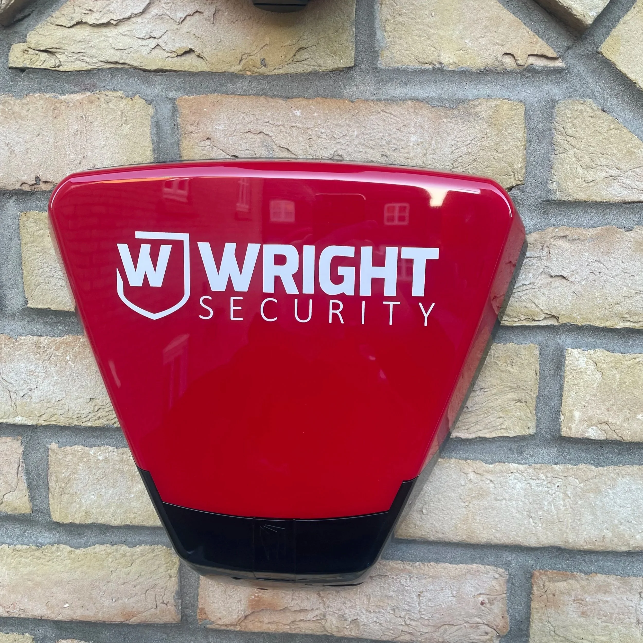 A red Wright Security alarm siren mounted on a brick wall.