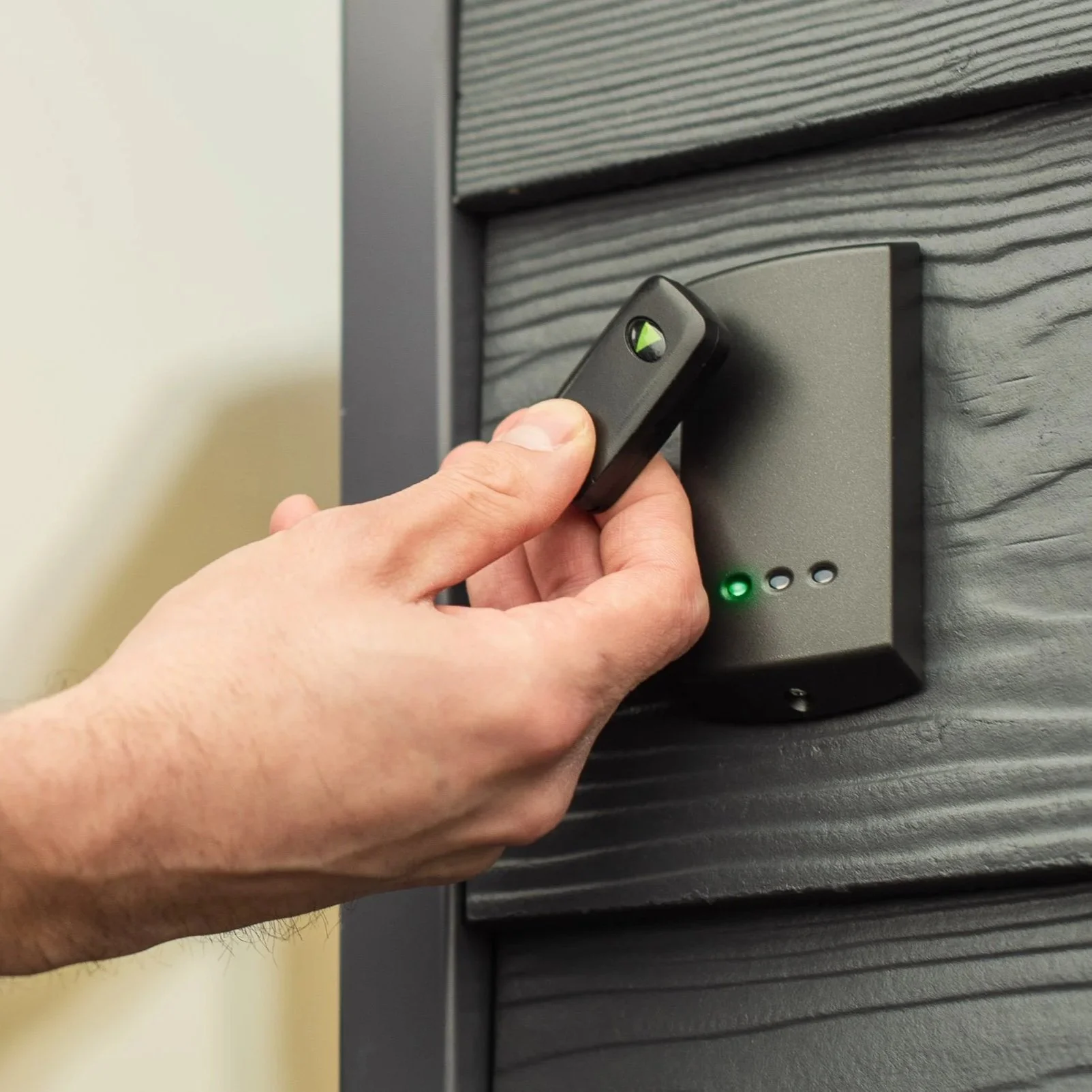 A person’s hand holding a remote control pressing a button on an electronic access keypad.