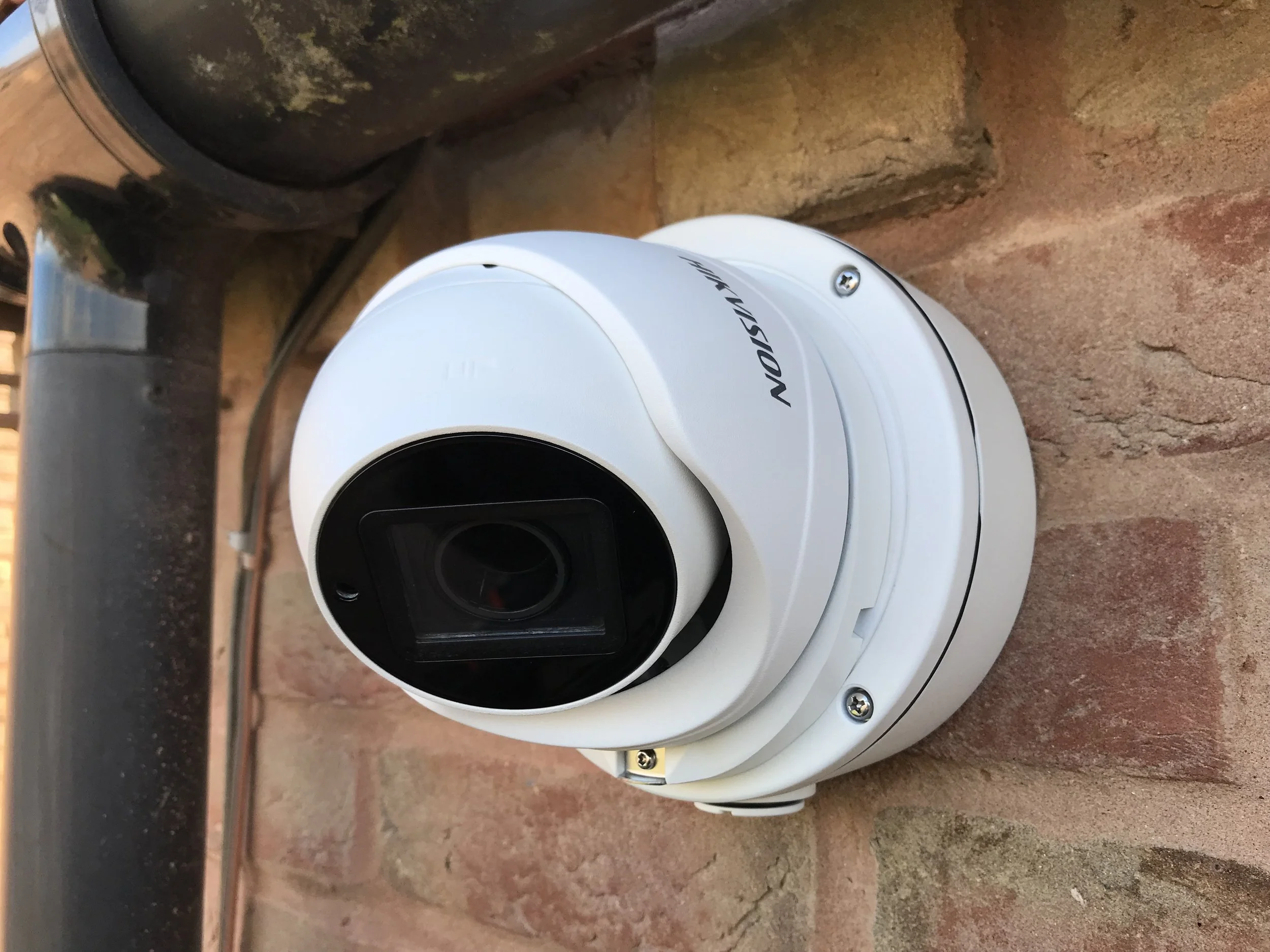 White security camera mounted on a brick wall, with a black cable nearby.