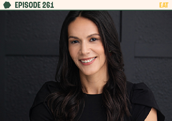 A woman with long dark hair smiling, wearing a black top, in front of a dark wall.