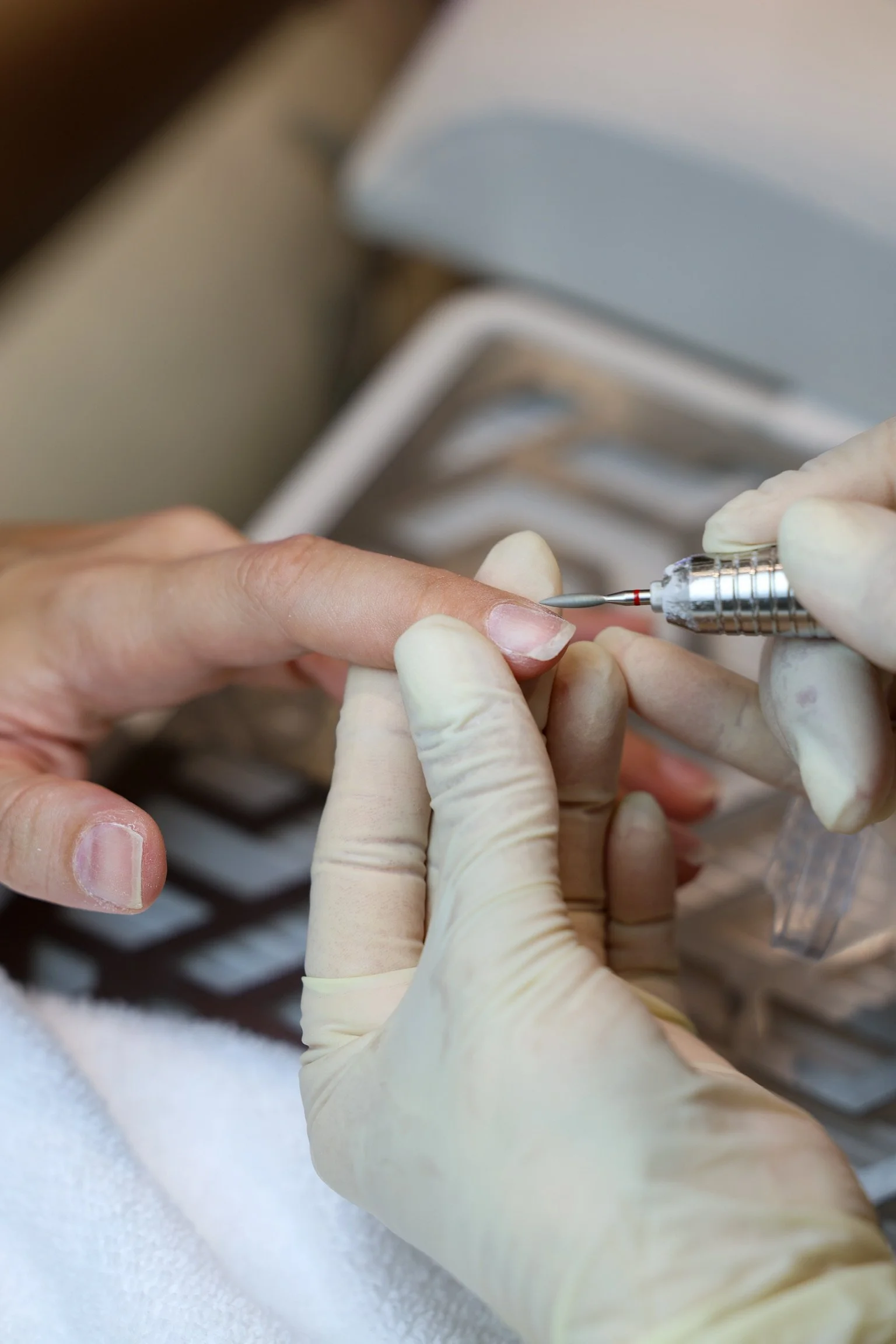 Close-up of a person getting a manicure, with a technician using an electric file on the person's fingernail.