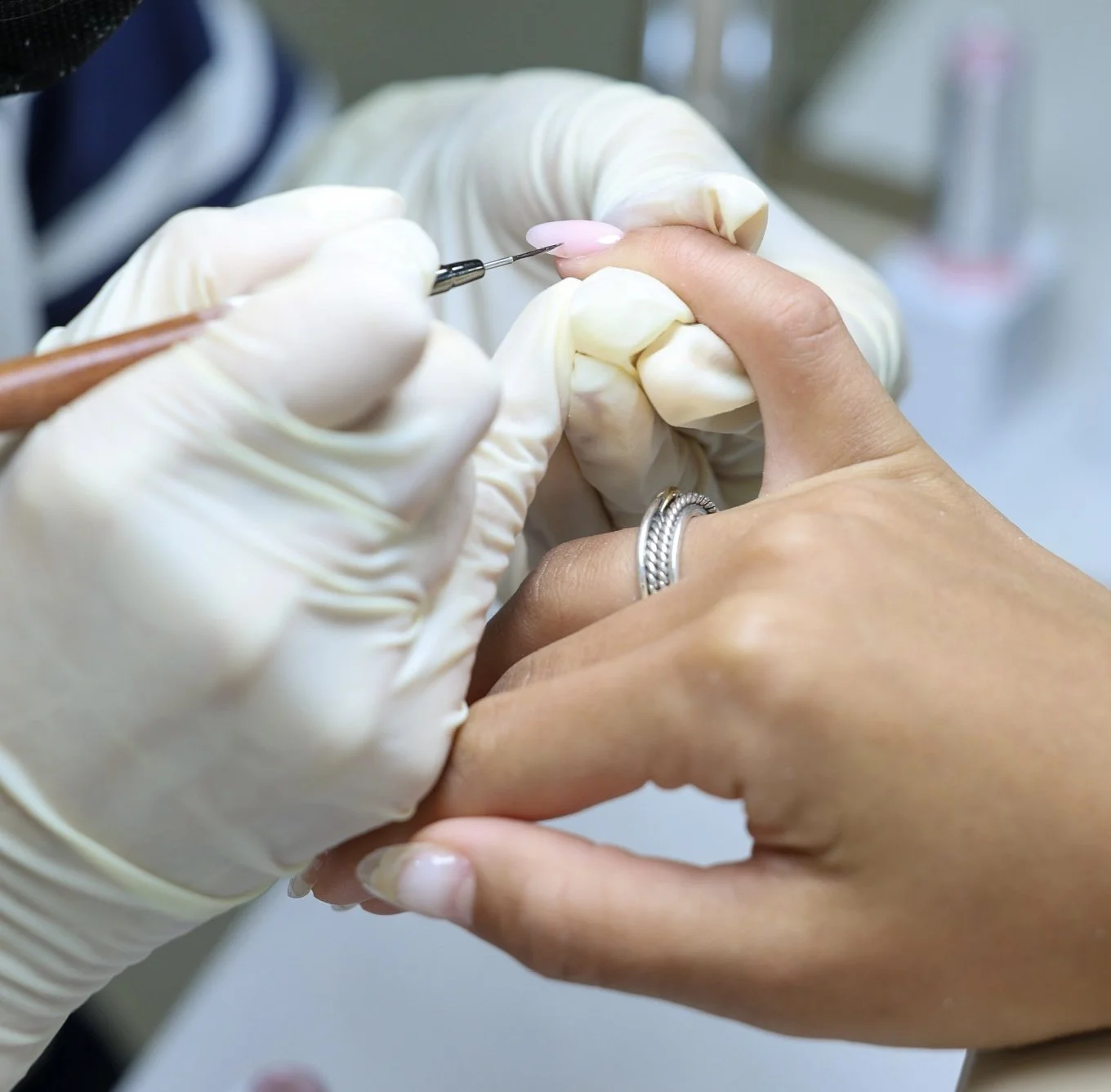 A person receiving a manicure with a dip powder nail application using a small brush, while wearing gloves.