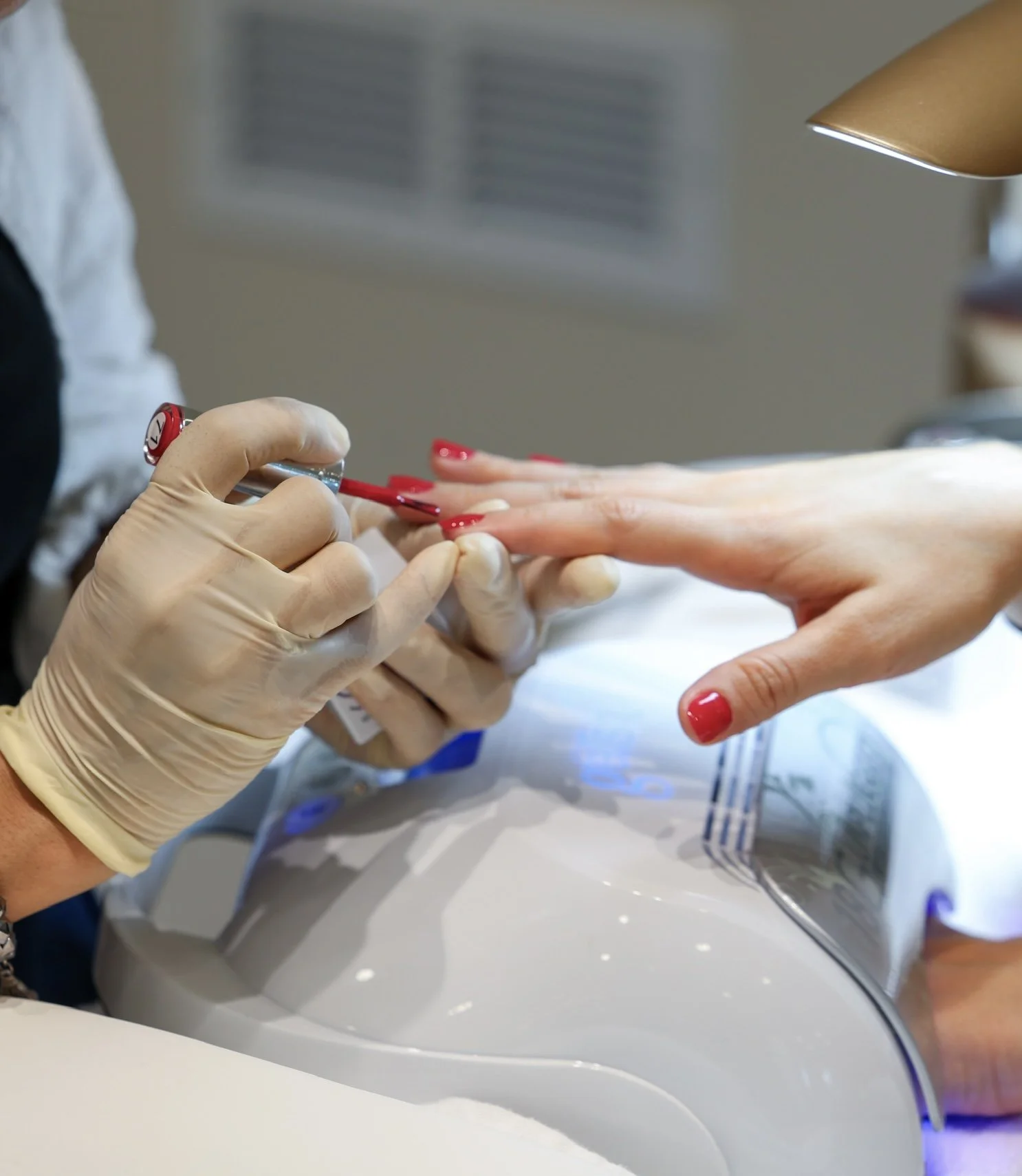 Close-up of a person receiving a manicure at a salon, with a nail technician applying red nail polish to a client's nails.