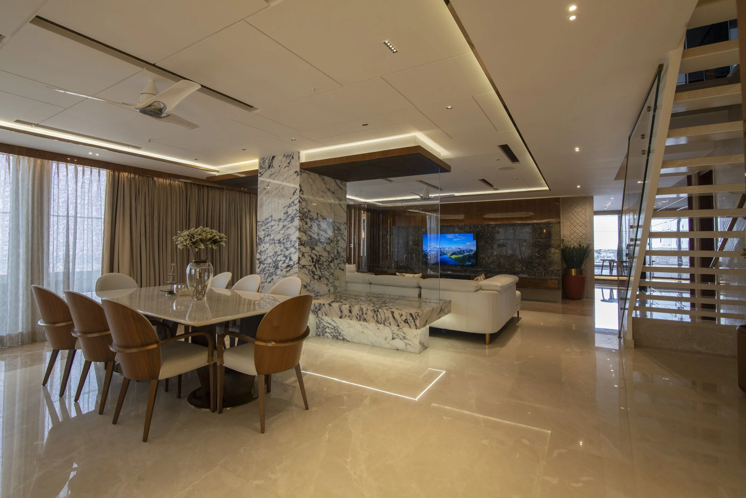 Modern living room and dining area with marble accents and beige tiled flooring.