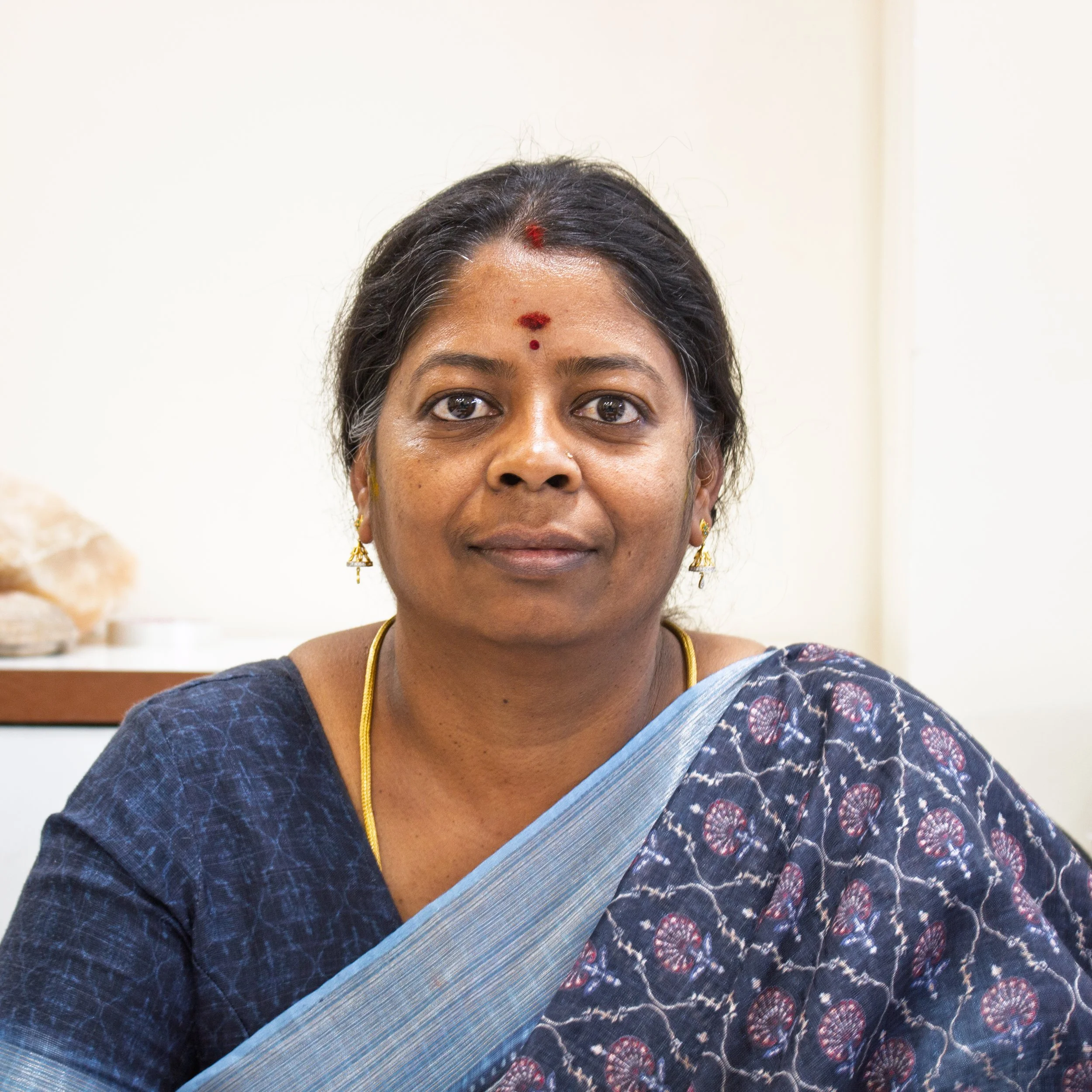 A young man sitting on a bench against a beige wall, wearing a gray polo shirt and light-colored pants, with a serious expression and shadow cast on the wall.