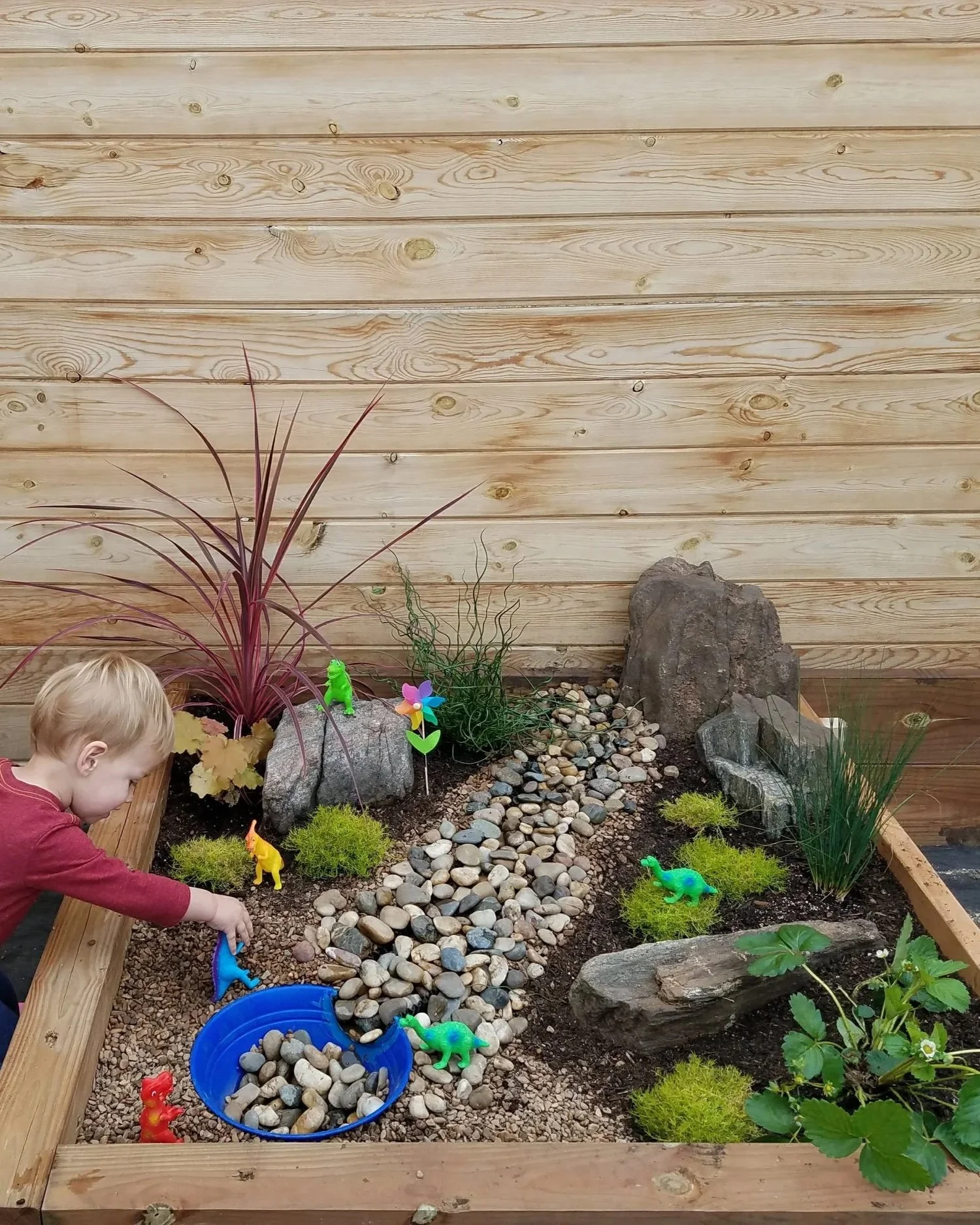 Child playing in a child's sensory garden with rocks and toys.