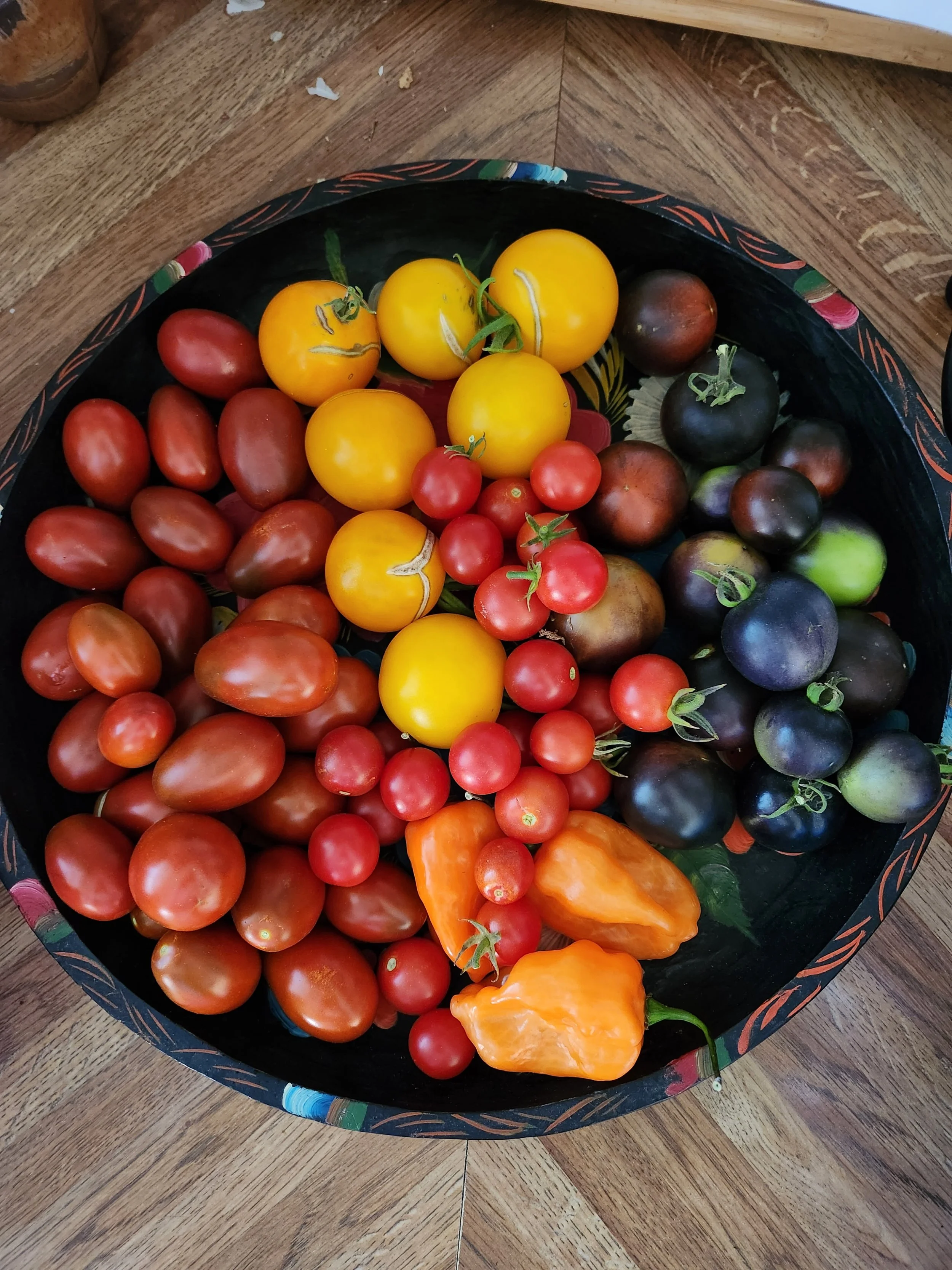 A basket of heirloom tomatoes in various colors including red, yellow, purple, and orange, placed on a wooden table.