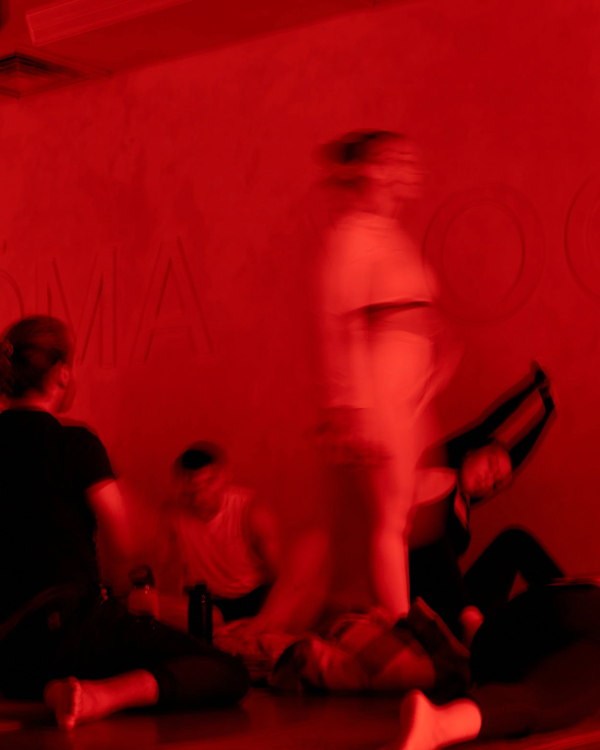 People sitting at a table under red lighting, some wearing hats, in a room with a wall that has partial text reading 'WO' and decorative elements.
