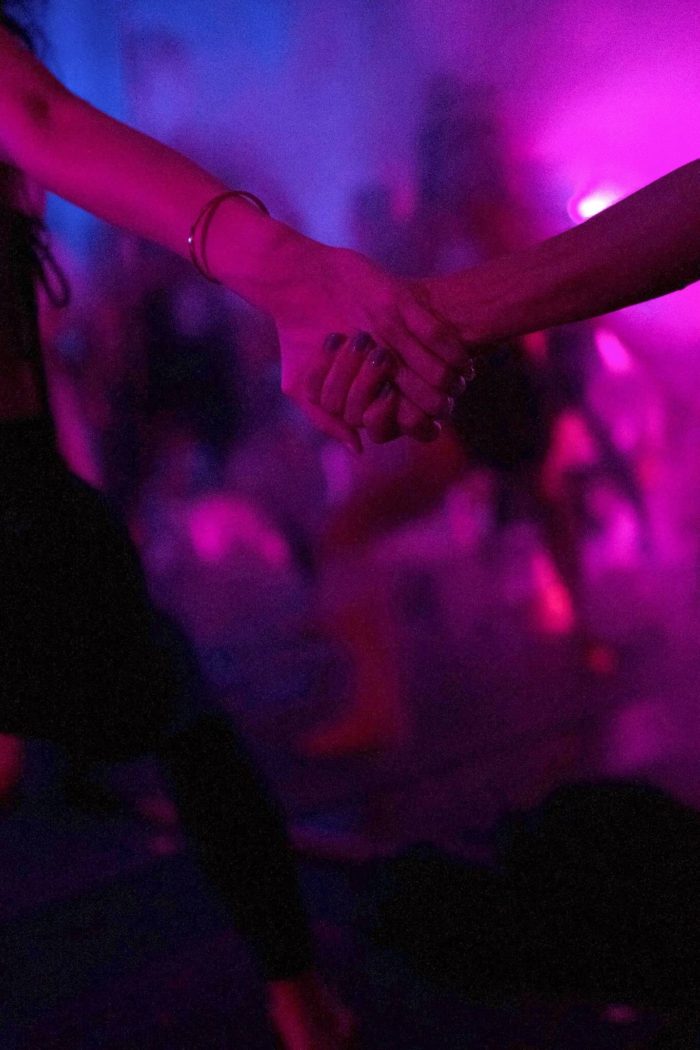 Two people holding hands in a dark setting illuminated by pink and purple lights.