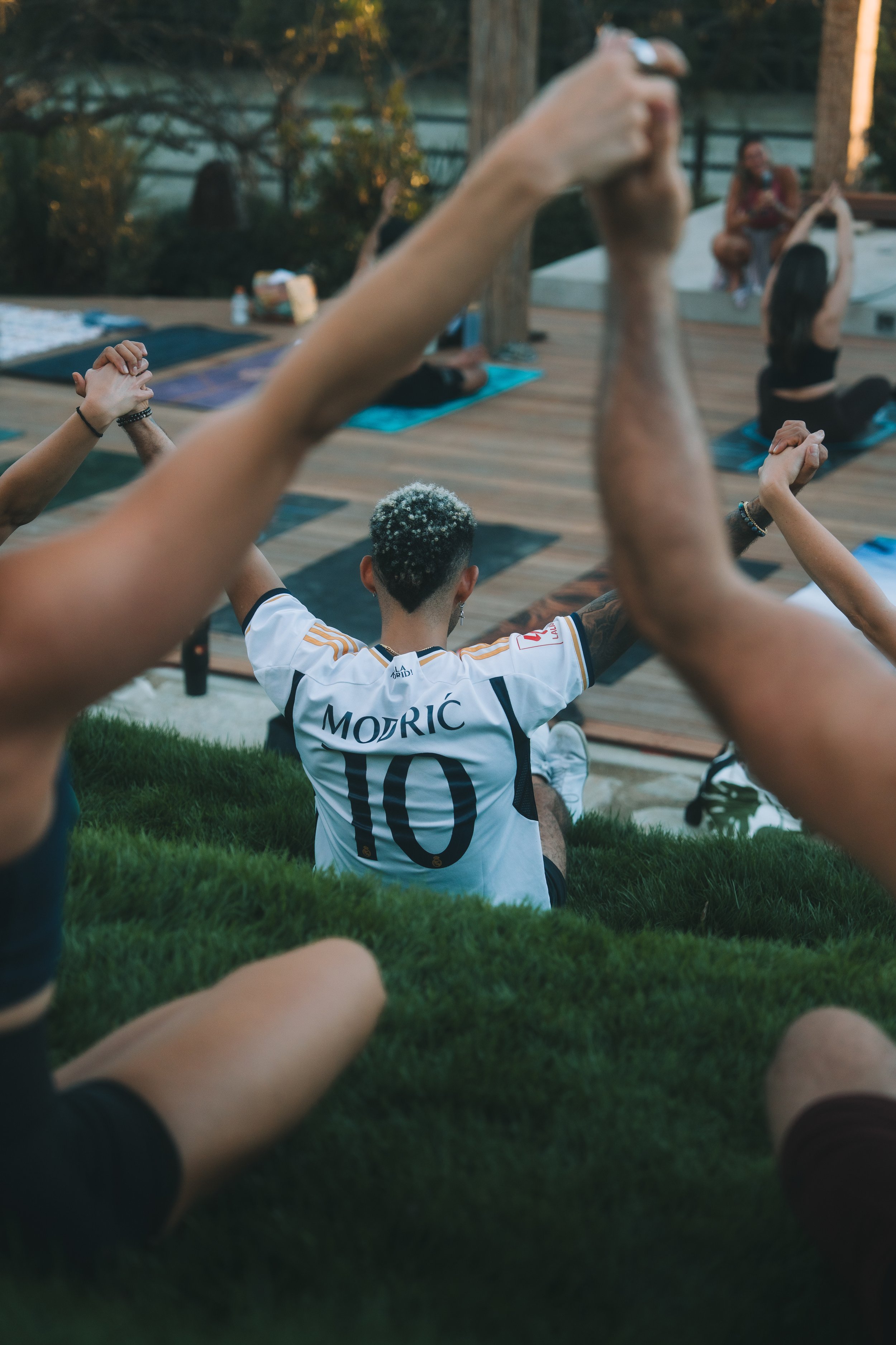 People practicing yoga outdoors on yoga mats, with a person wearing a soccer jersey that has the name 'MORIC' and the number '10' on the back.