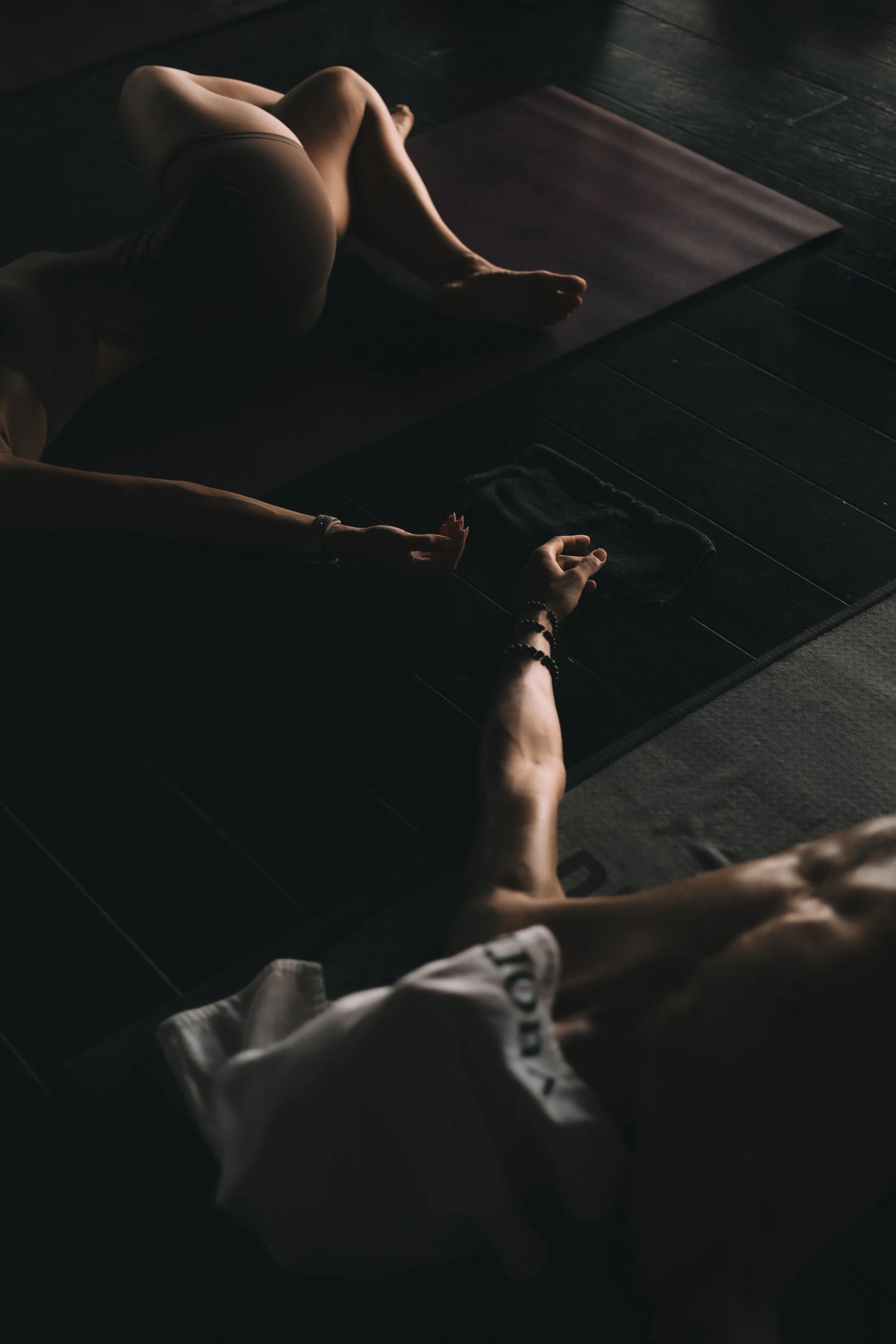 A person practicing yoga or meditation on a yoga mat in a dimly lit room with dark wooden floors.