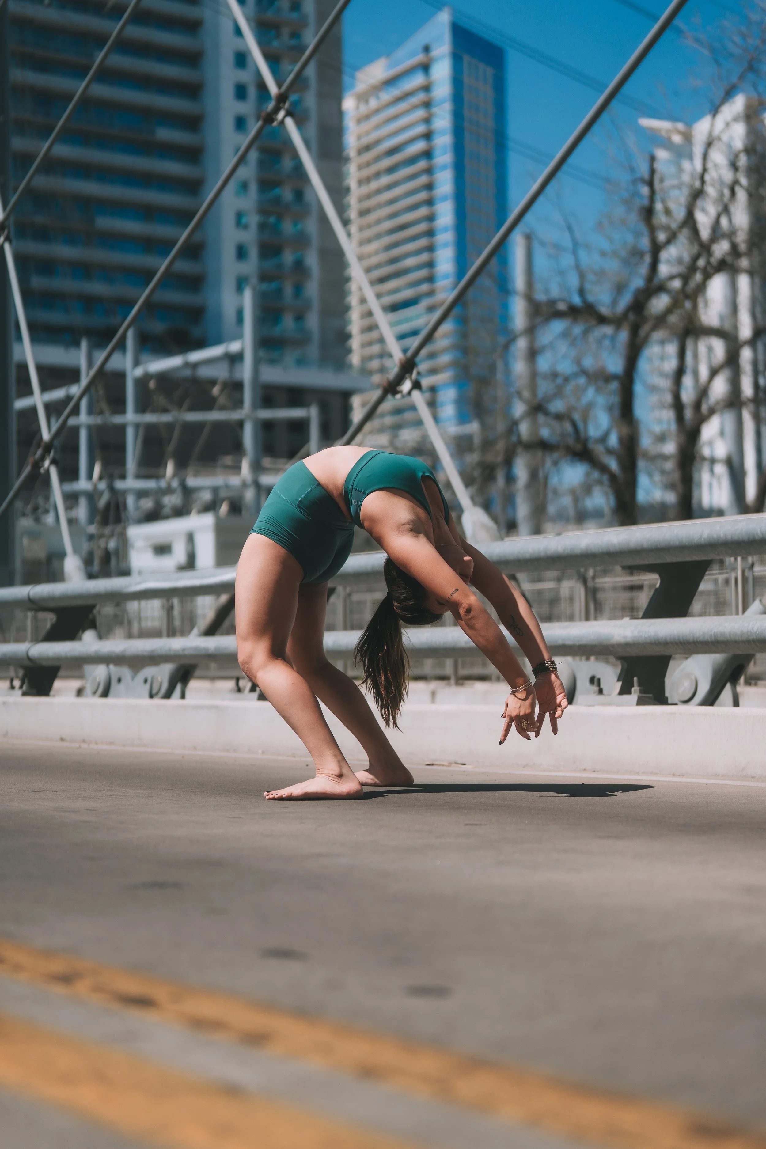A woman performing a yoga pose on a city street during daytime with high-rise buildings and trees in the background.