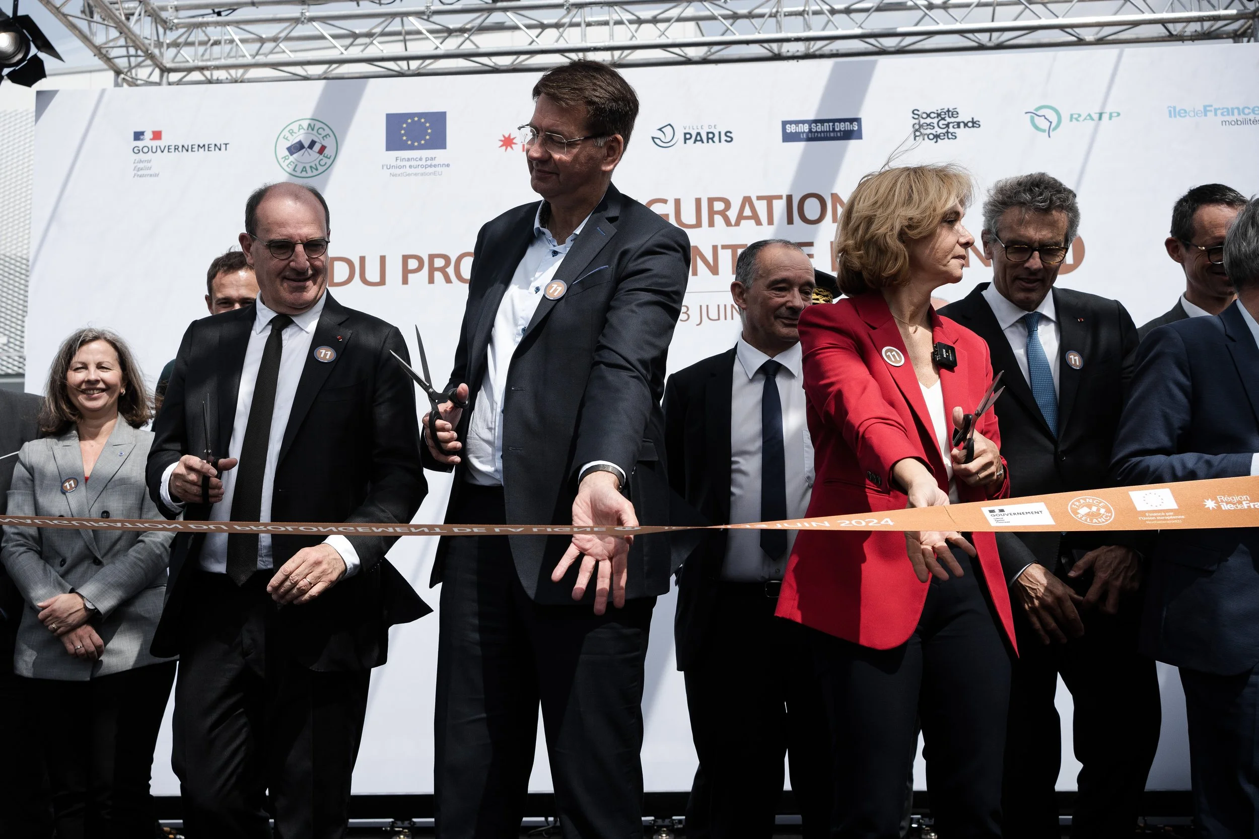 Groupe de personnes lors d'une cérémonie de coupe de ruban, certains tenant des ciseaux, en tenue formelle, devant une bannière avec divers logos.