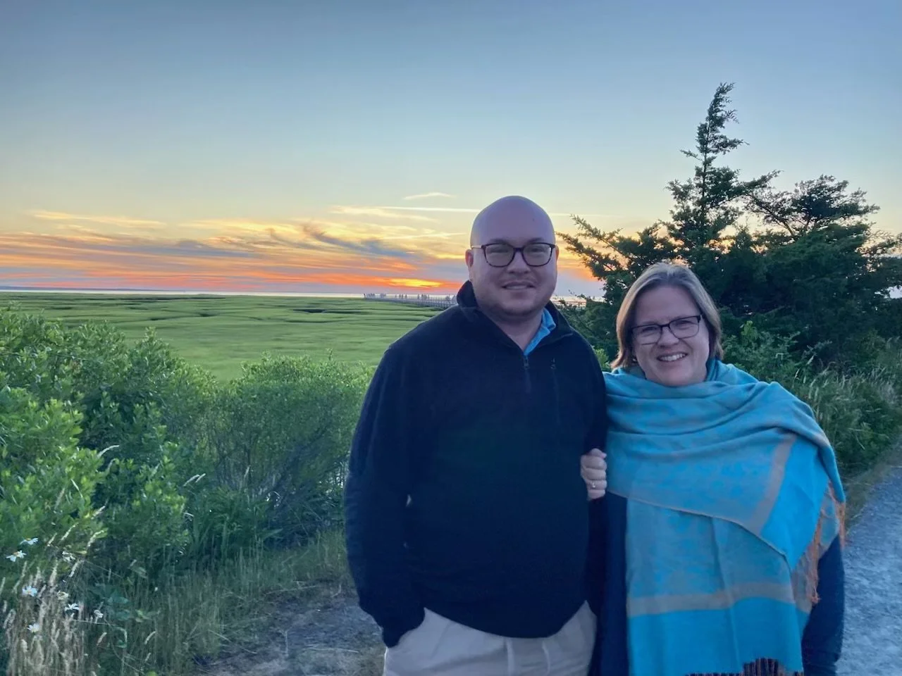 Mo and his partner smiling and standing together outdoors at sunset
