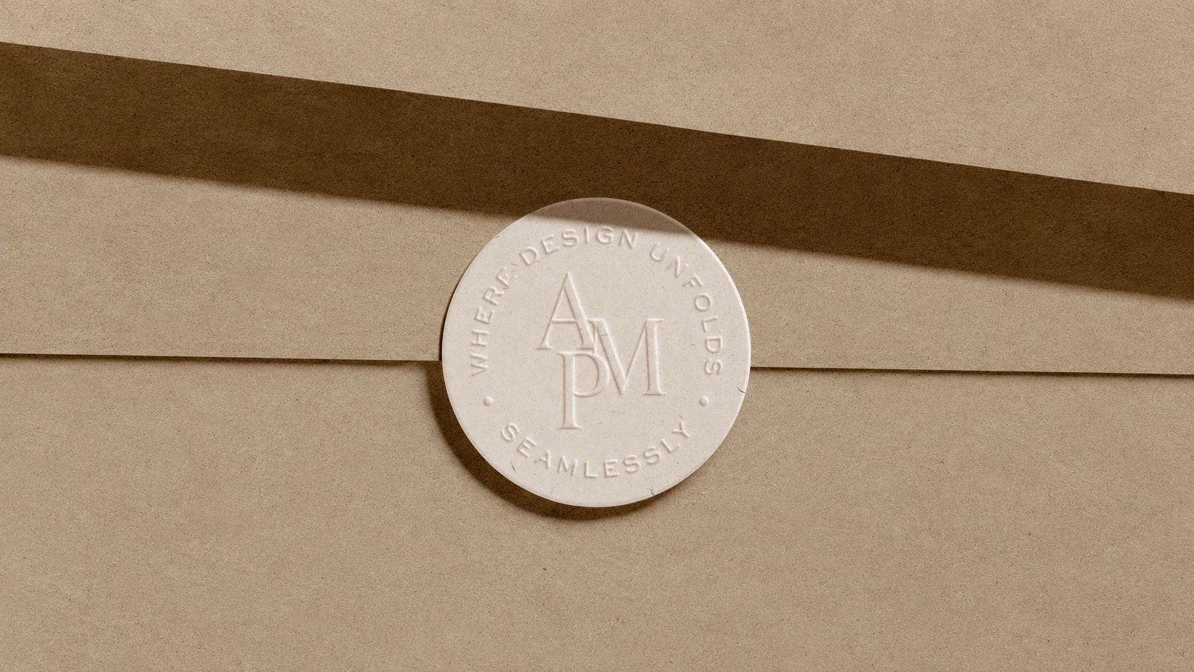 A white circular sticker with embossed text that reads "WHERE DESIGN UNFOLDS SEAMLESSLY" and contains the initials 'APM' in the center, affixed on a tan-colored paper surface.