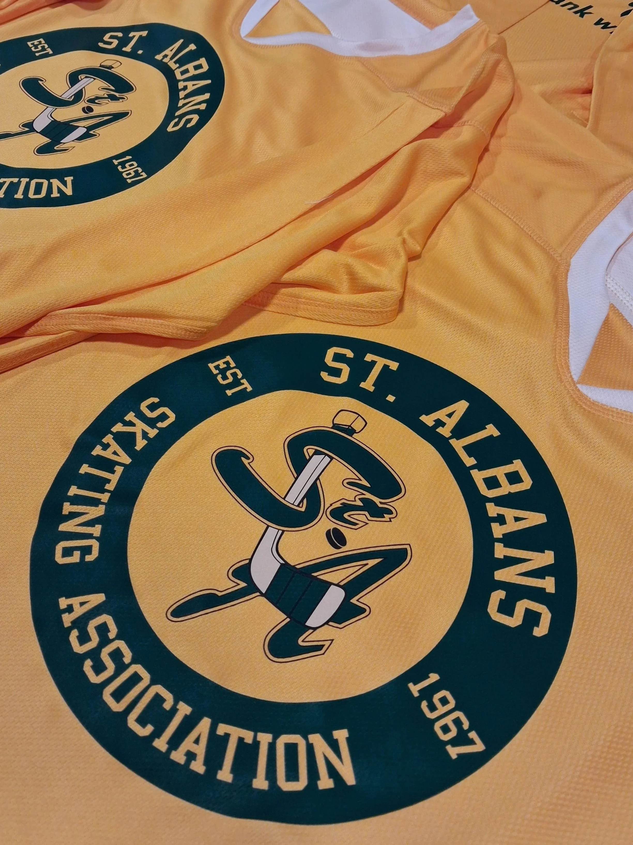 Close-up of yellow sports jerseys with a circular logo featuring a microphone wrapped with a pencil and text surrounding it.
