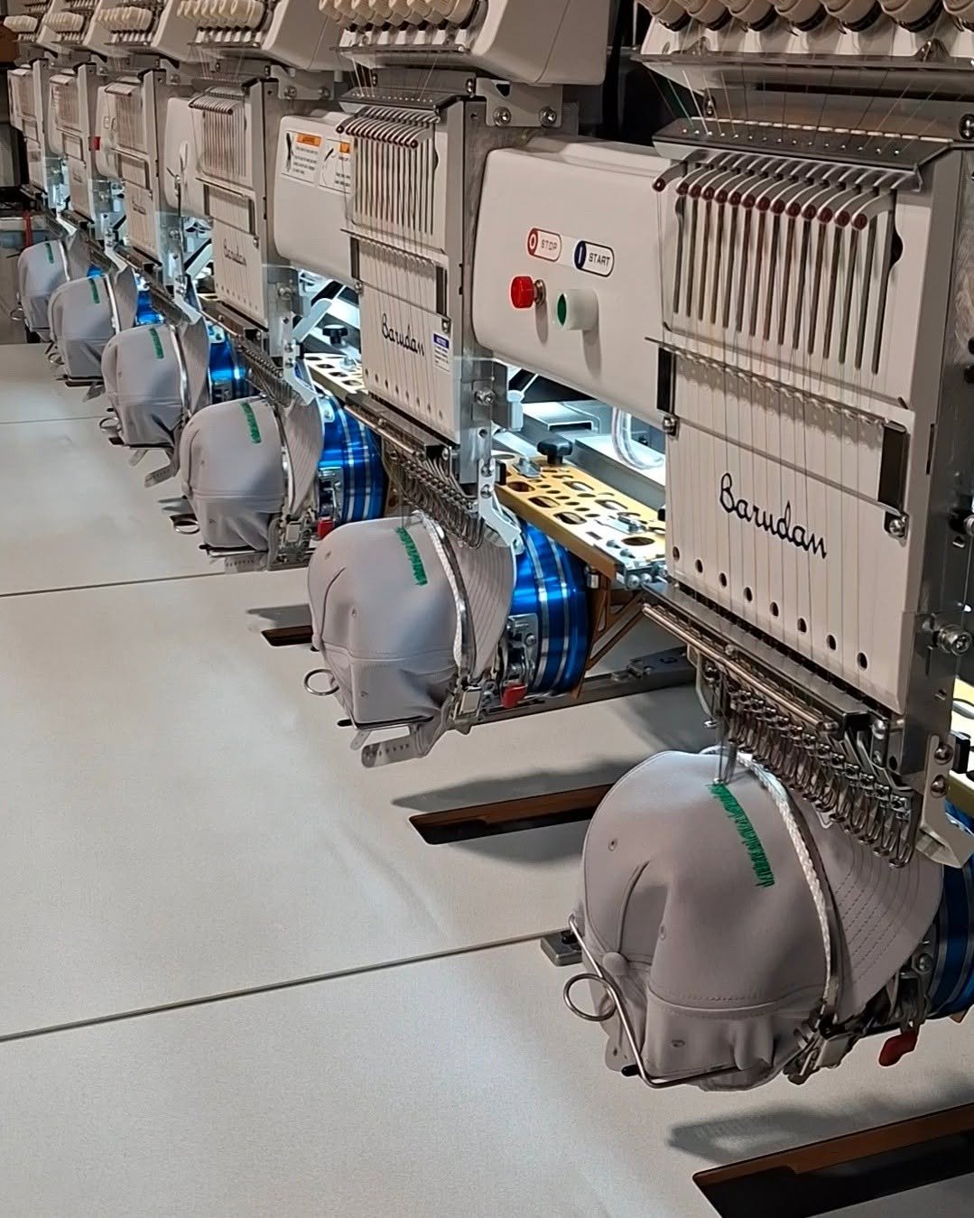 Industrial embroidery machines sewing fabric caps in a factory setting.