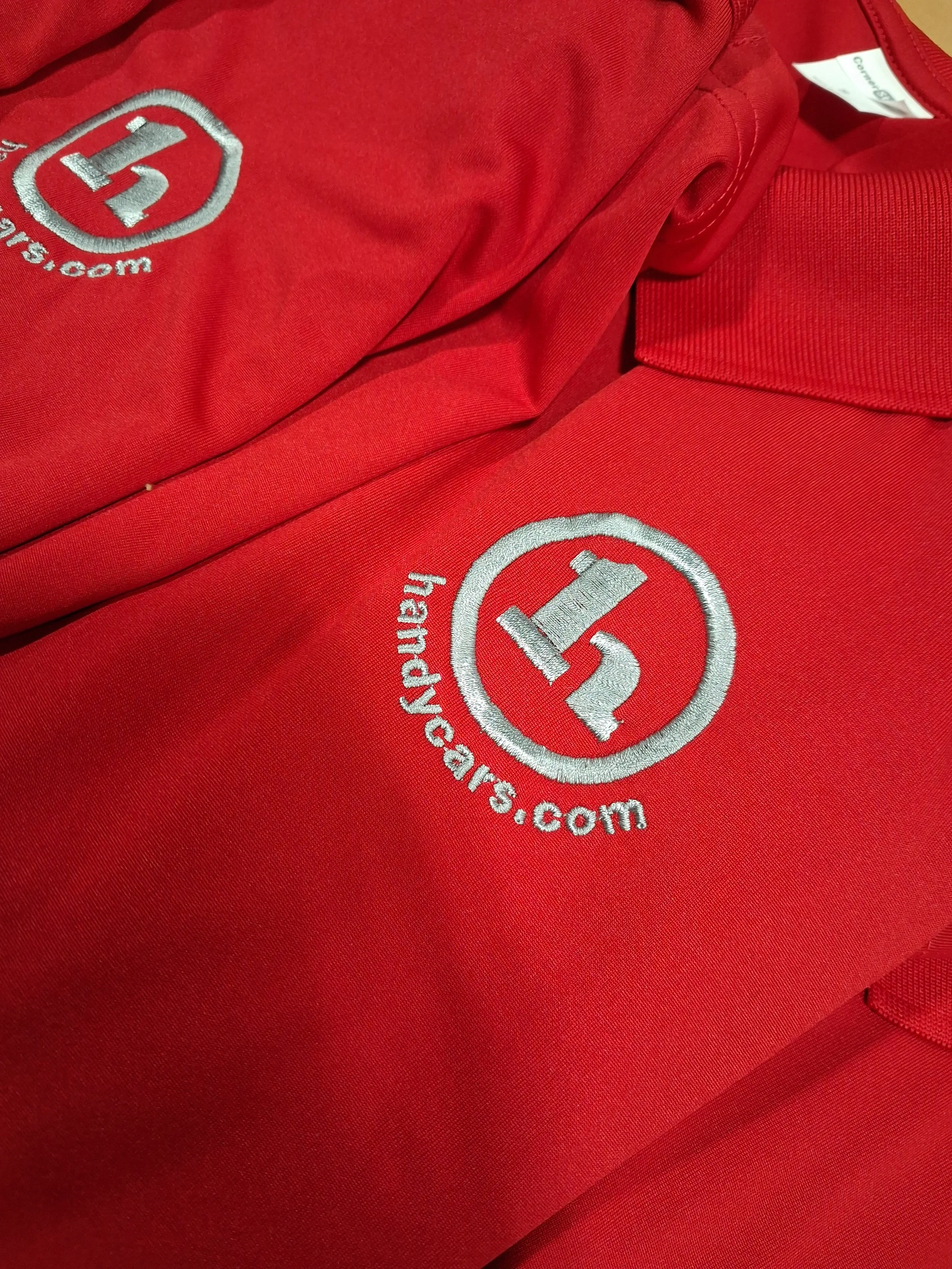 Close-up of a red shirt with a white embroidered logo and website URL.