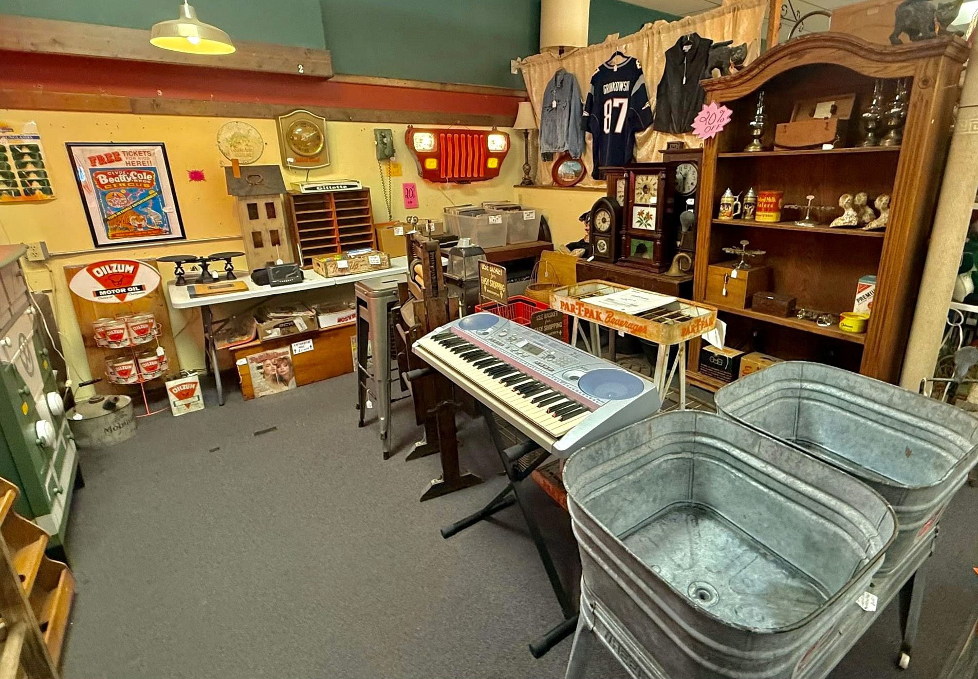 Interior of a thrift store with various vintage items, including a keyboard, metal tubs, a wooden shelf with figurines, clothing, and signs, under warm lighting.