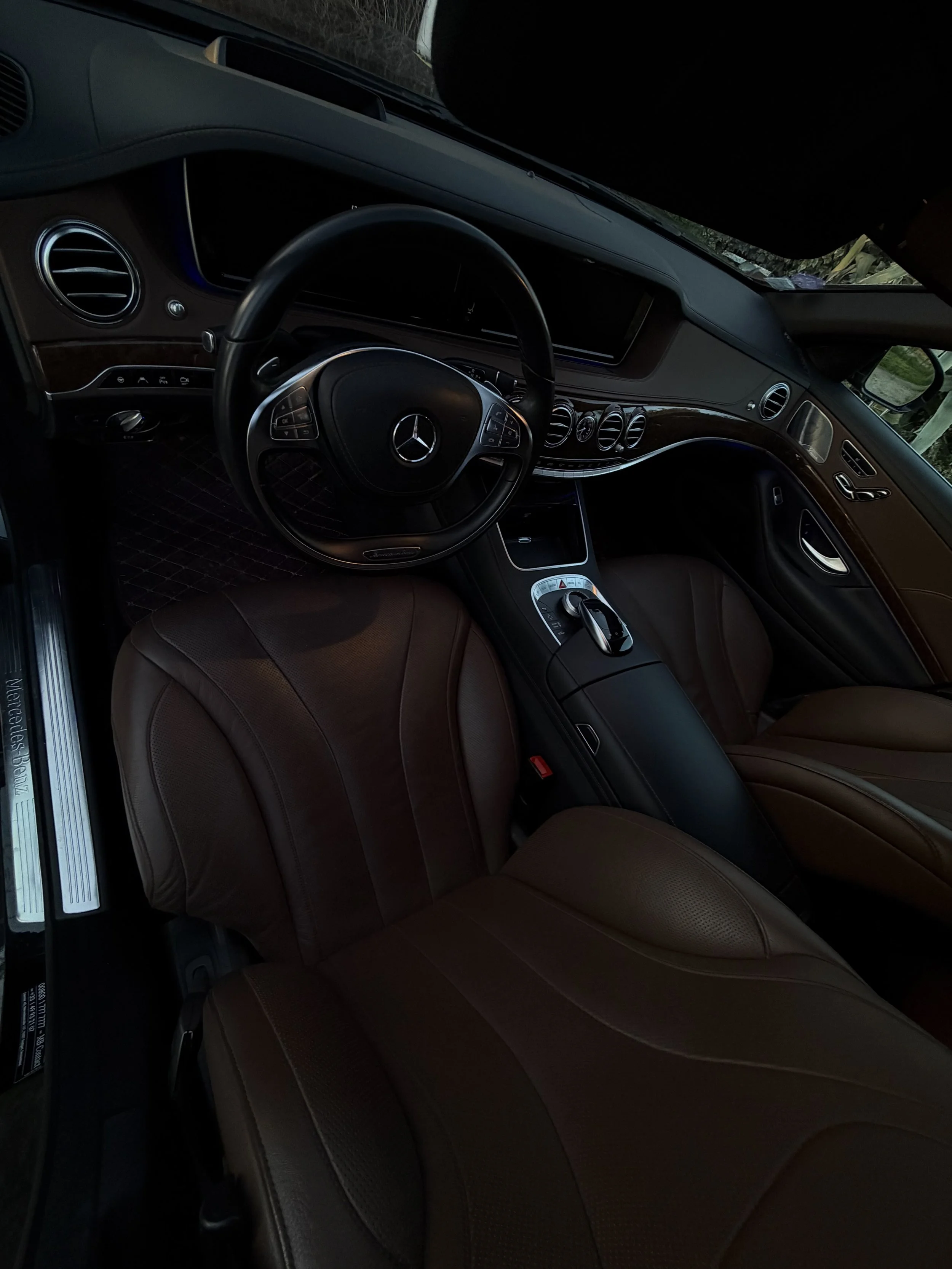 Intérieur d'une voiture de luxe Mercedes-Benz avec des sièges en cuir marron, un volant avec le logo Mercedes, et un tableau de bord sophistiqué.